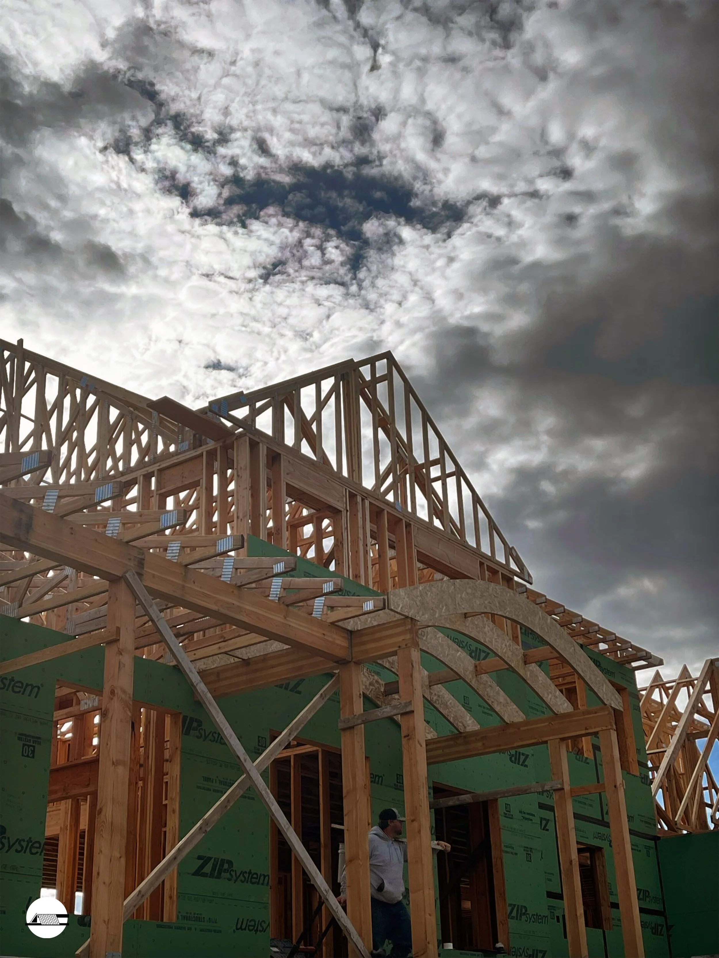 Wooden framing and sheathing of a house under construction with cloudy sky overhead.