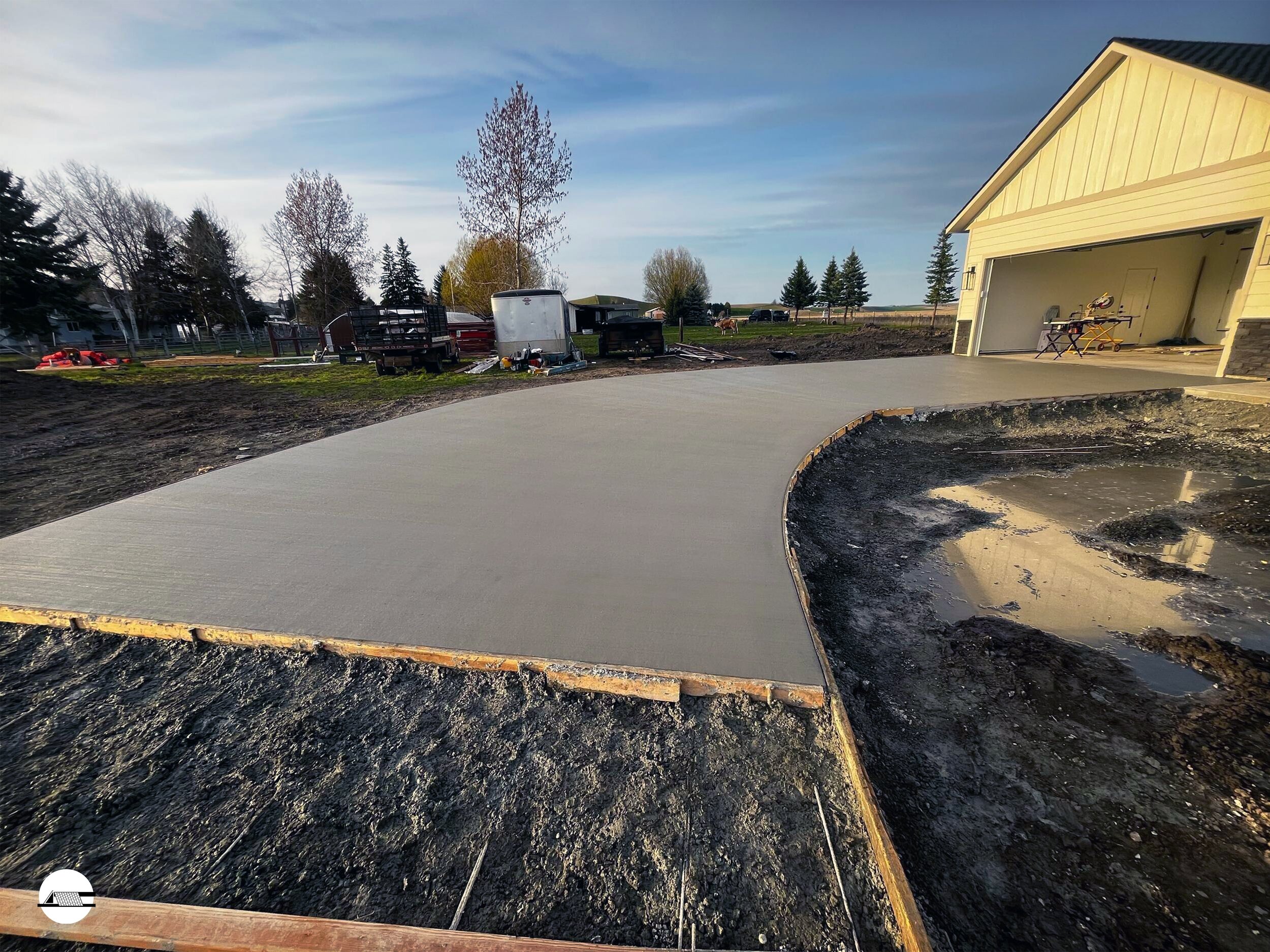 Freshly poured concrete driveway in front of a garage with construction tools and equipment nearby, in a rural residential area.