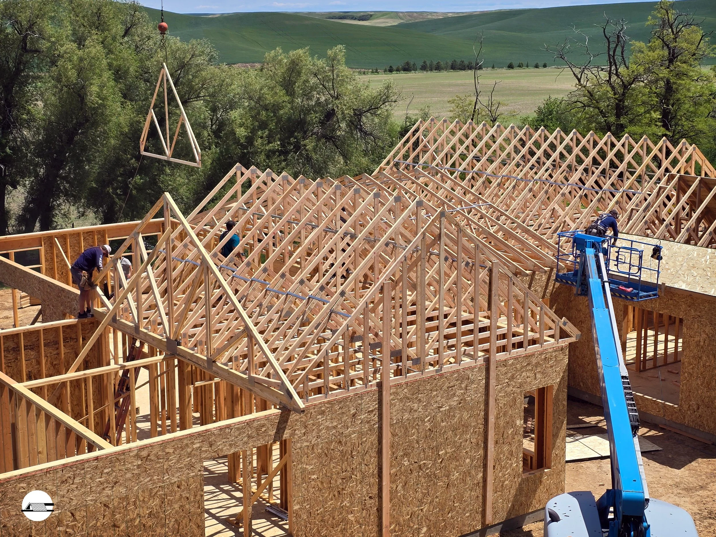 Constructing a house with wooden framing and roof trusses in a rural area with green rolling hills in the background.