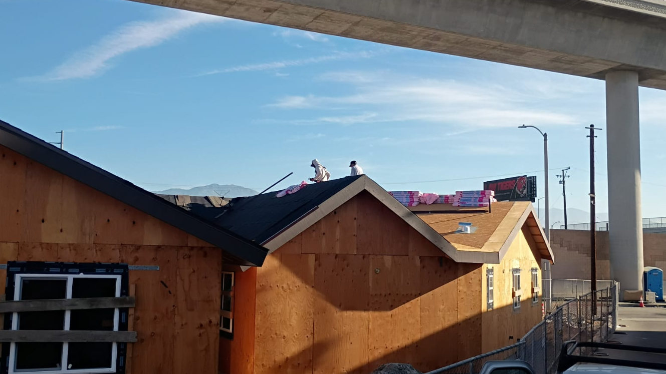 Roofing work in progress above newly sheathed exterior walls