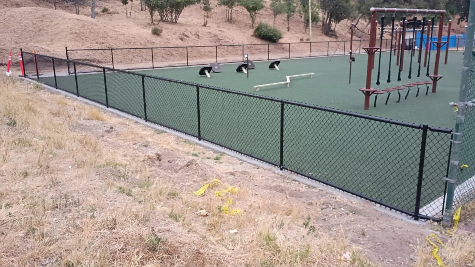 Wide view of the fenced obstacle course with balance and suspended stepping features.