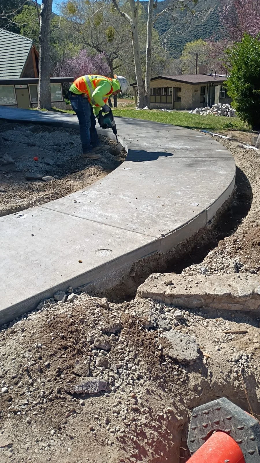 Worker using a power tool along the edge of the curved concrete walkway.