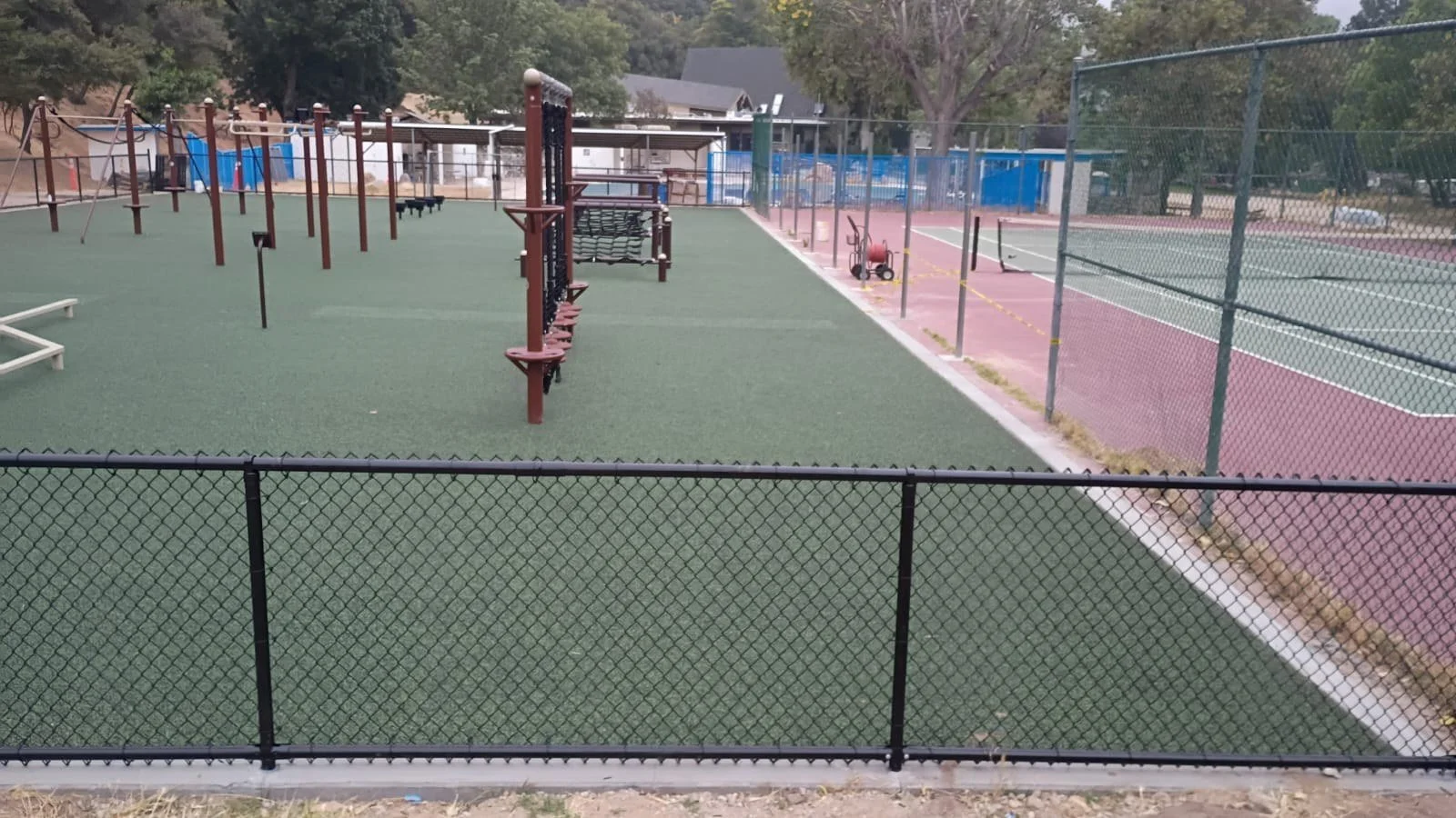 Obstacle course and climbing features beside an existing tennis court.