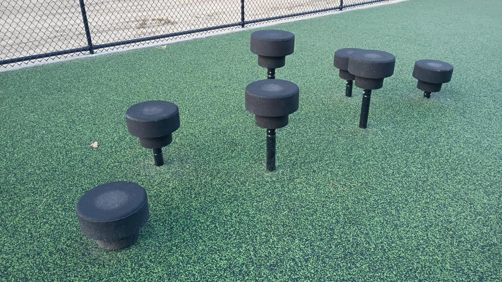 Black stepping platforms at staggered heights on green obstacle course surfacing.