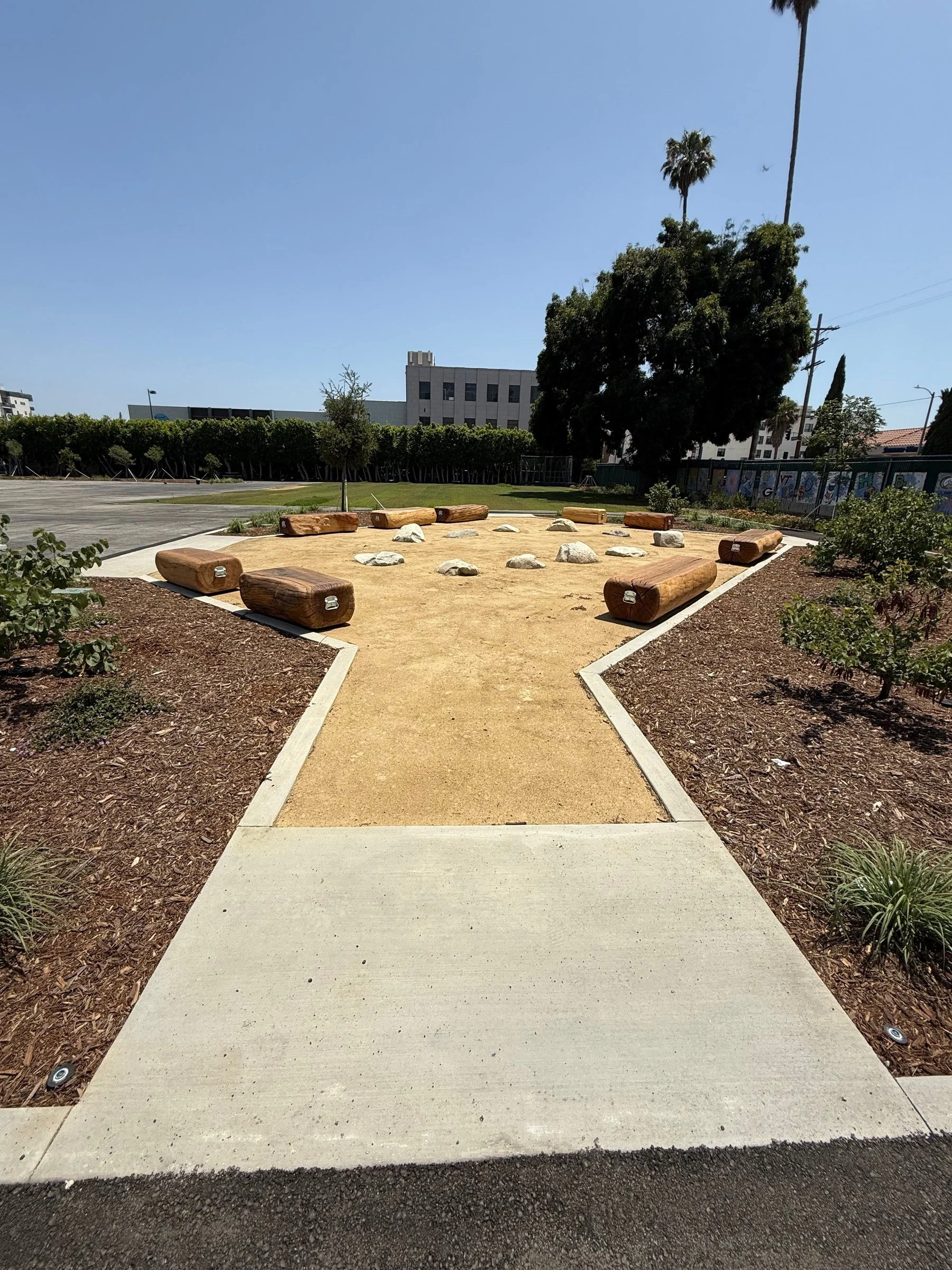 Completed schoolyard gathering area with log seating, rocks and landscaped paths.