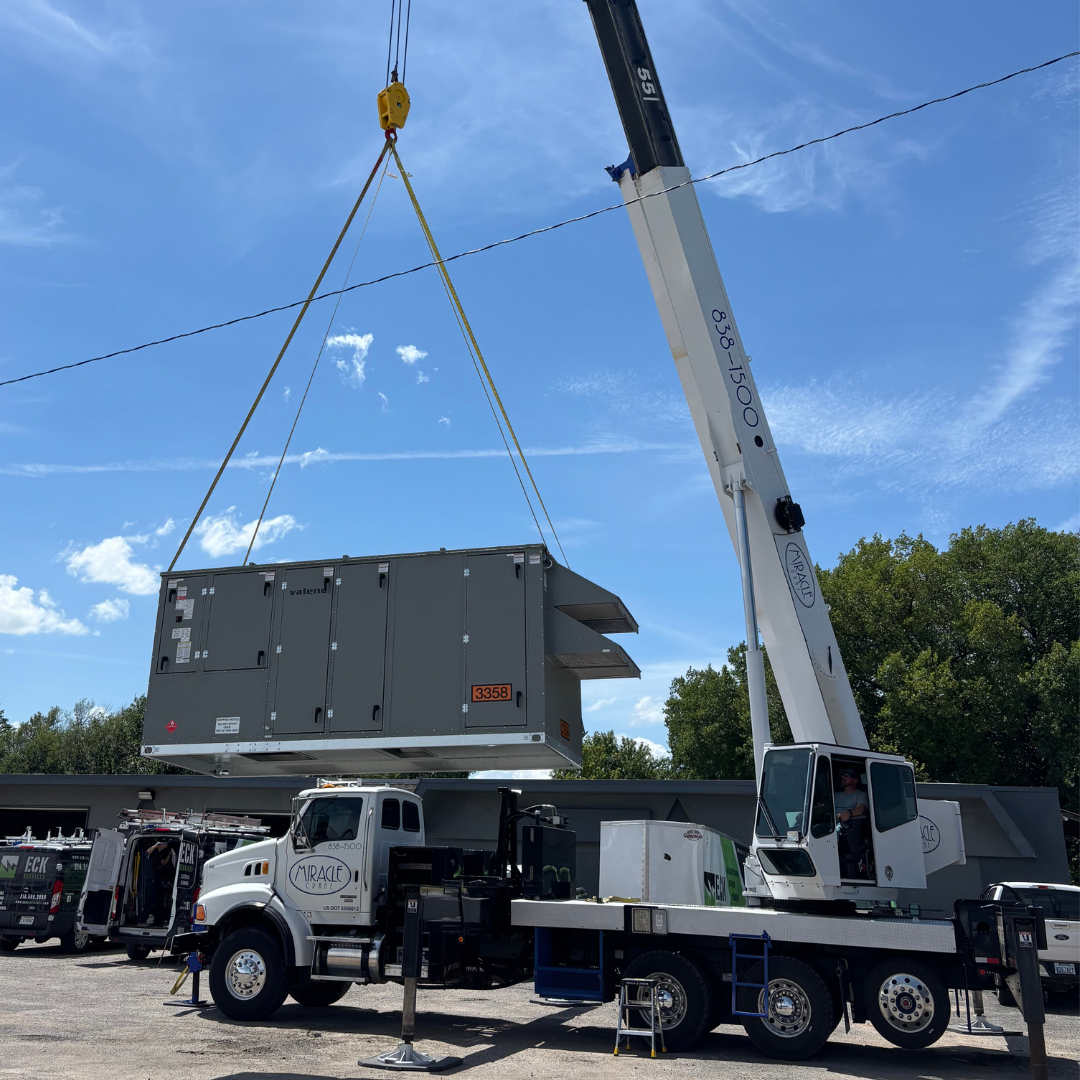 Mobile crane lifting large commercial rooftop HVAC unit in Wichita Kansas