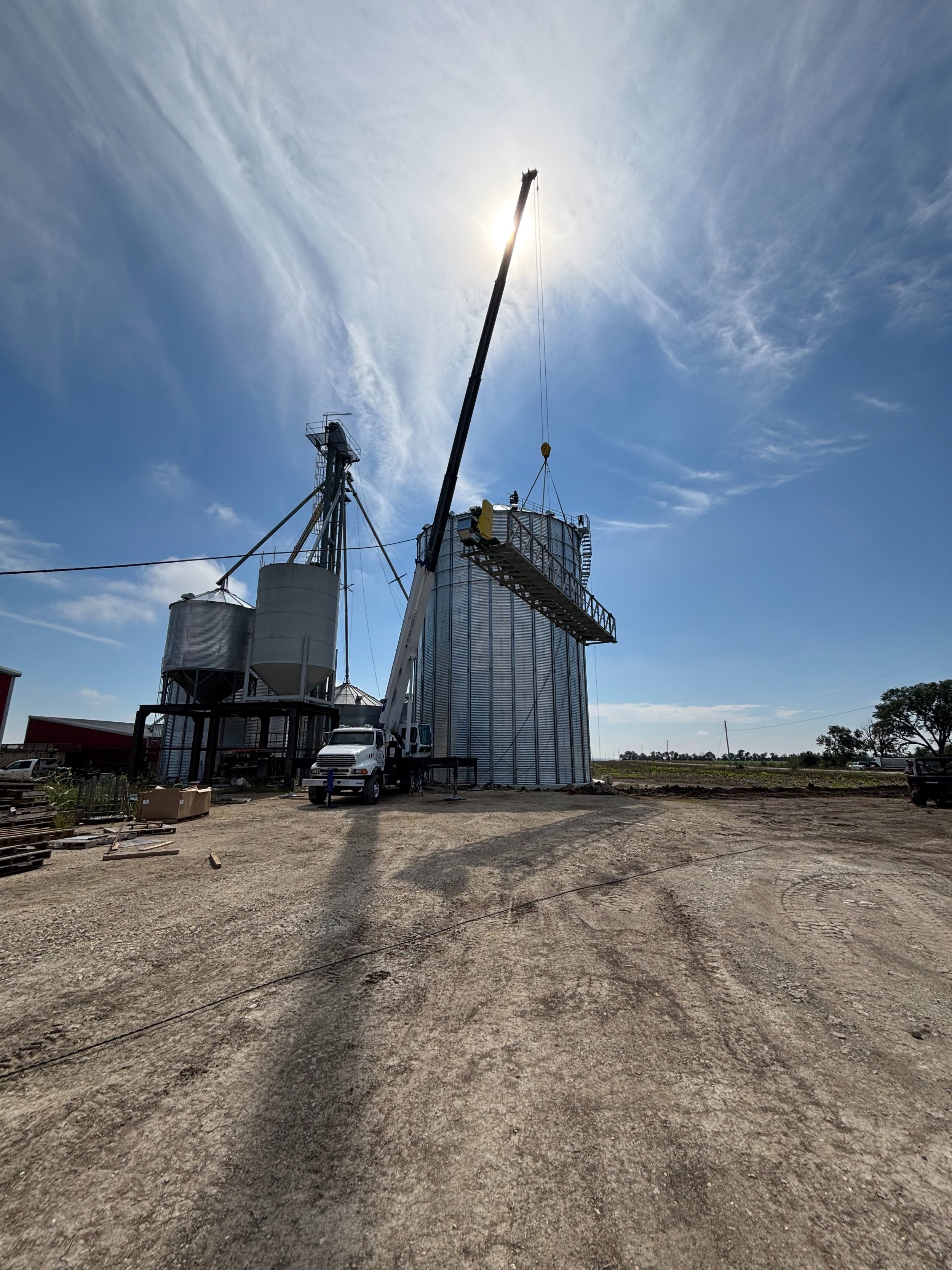 Miracle Crane's mobile crane hoisting a conveyor catwalk spout on top of metal grain silo at agricultural site in Newton, Kansas