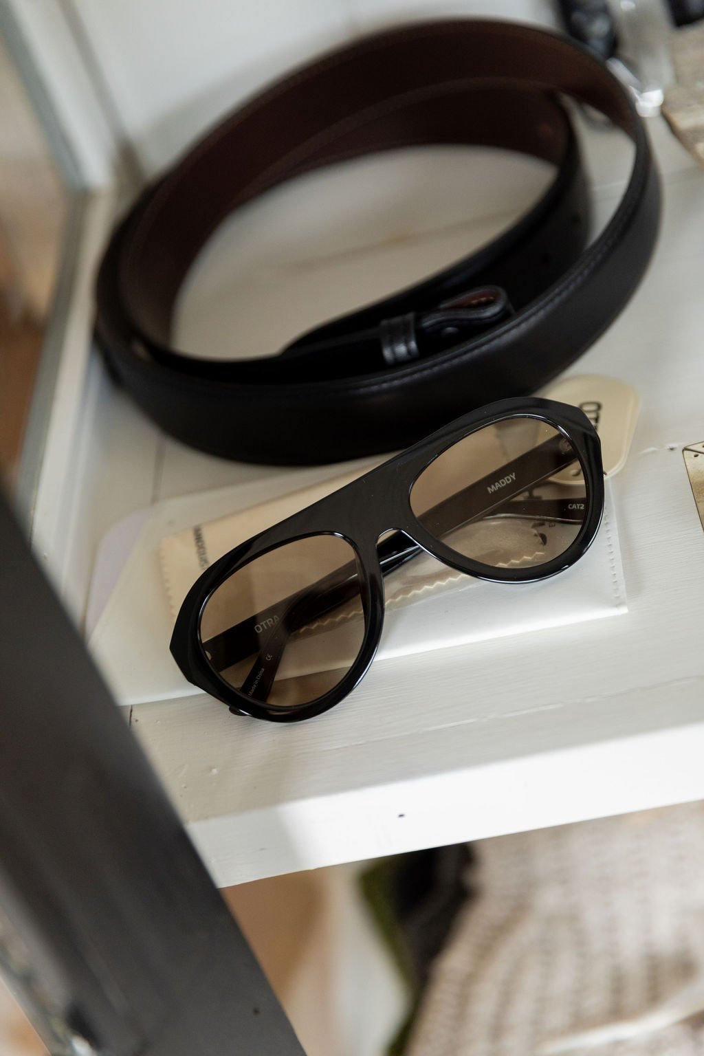 Pair of black sunglasses with a case behind them on a white surface, with cleaning cloths nearby.