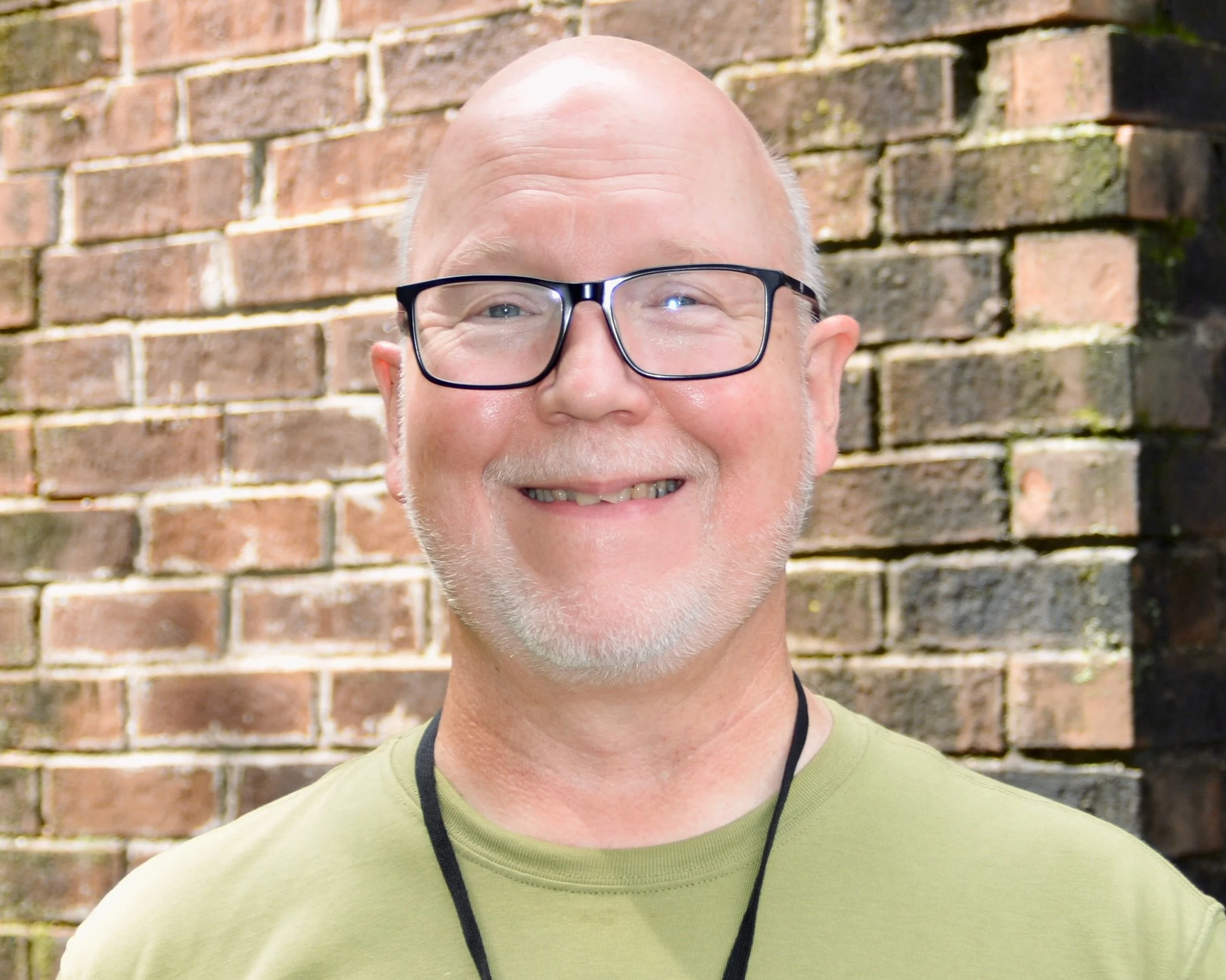 Profile of an older man with a bald head, wearing glasses and a blue striped shirt.