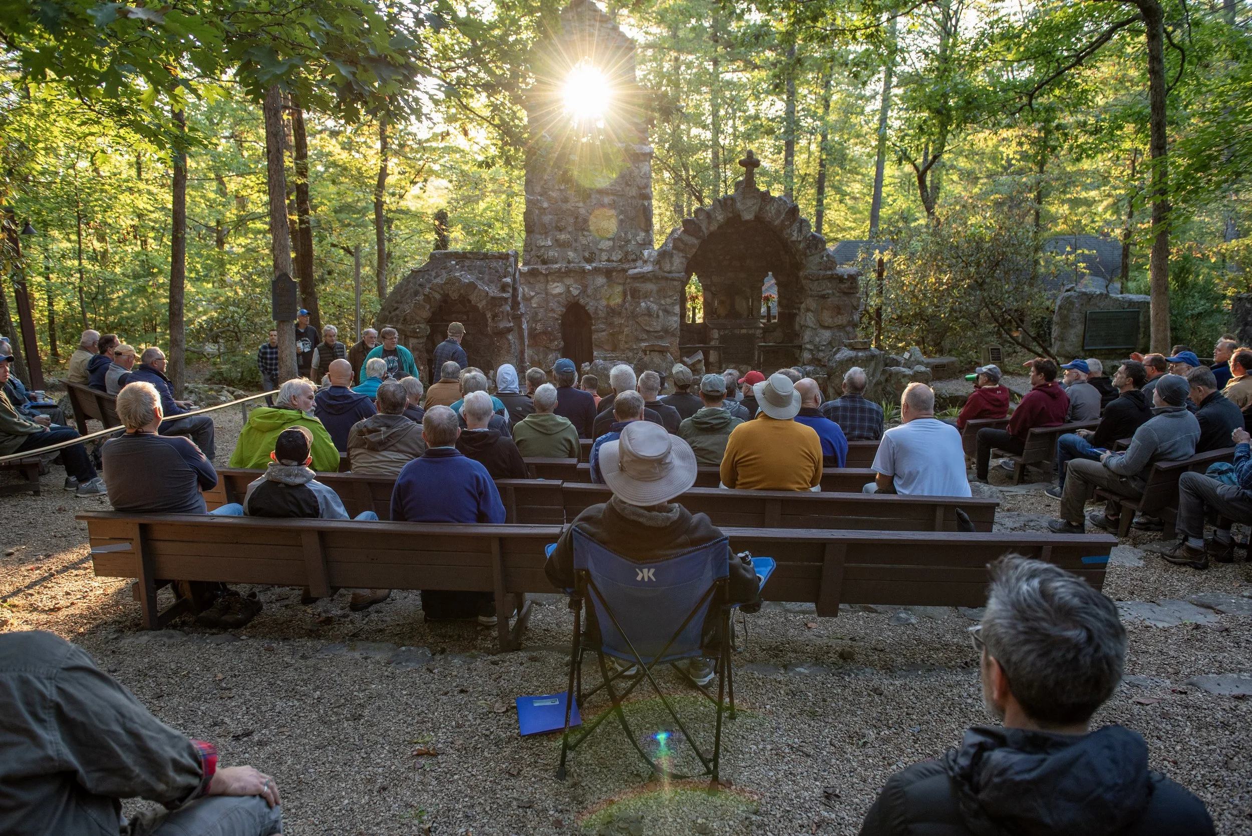 Outdoor gathering at a stone altar with sunlight filtering through trees