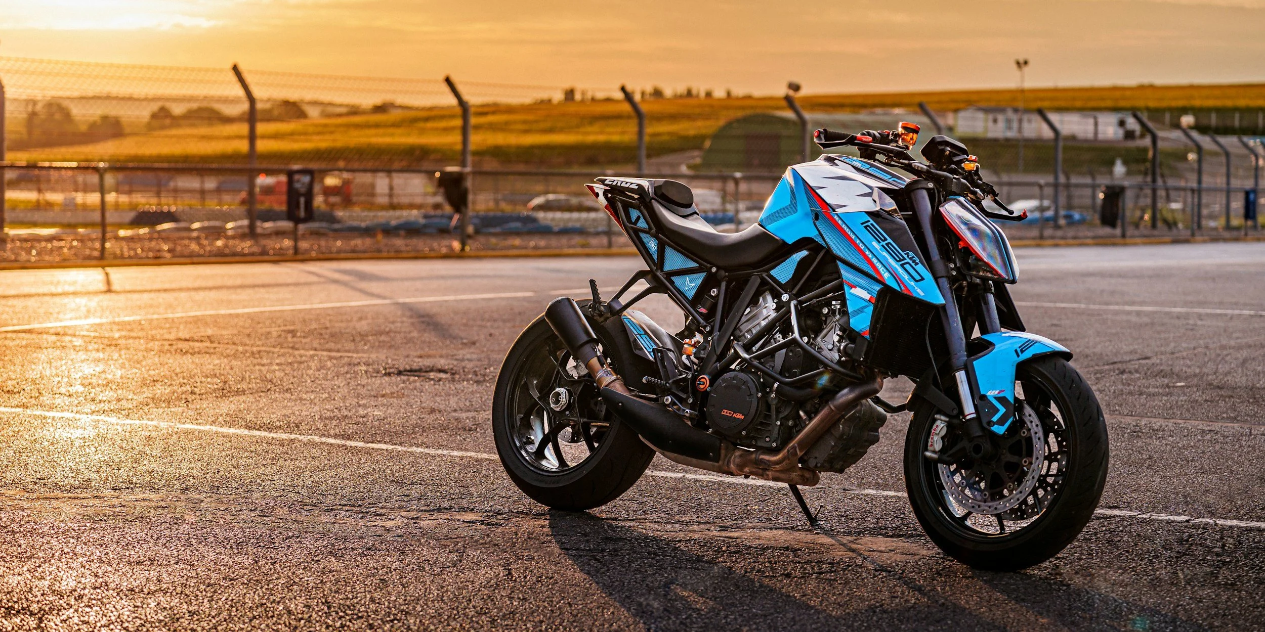 Blue and black motorcycle parked on an empty racetrack at sunset.