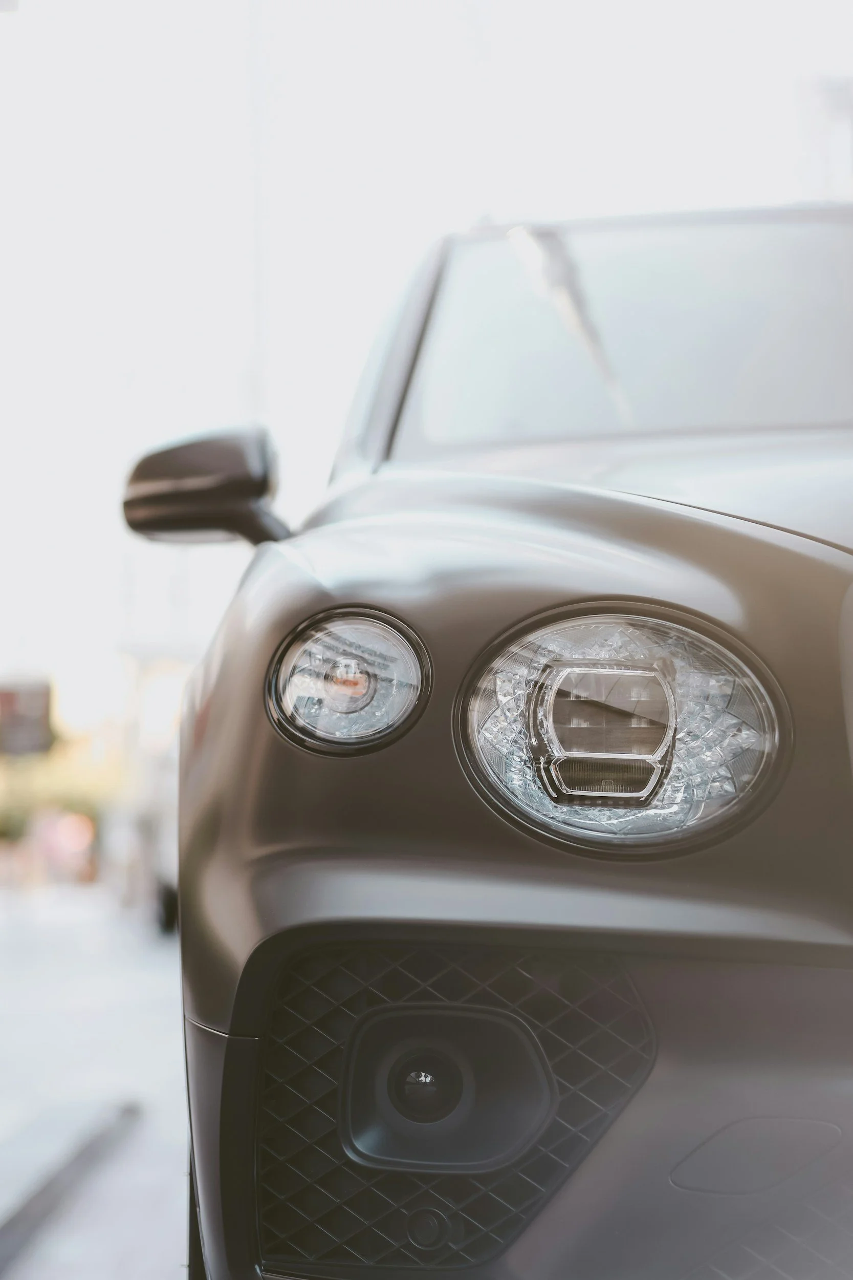 Close-up of a modern car's front left side, showing the headlamps, side mirror, and part of the grille.