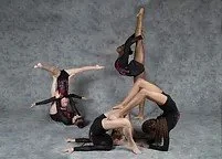 Three women in black and red costumes performing a synchronized gymnastic or dance pose on a gray floor.