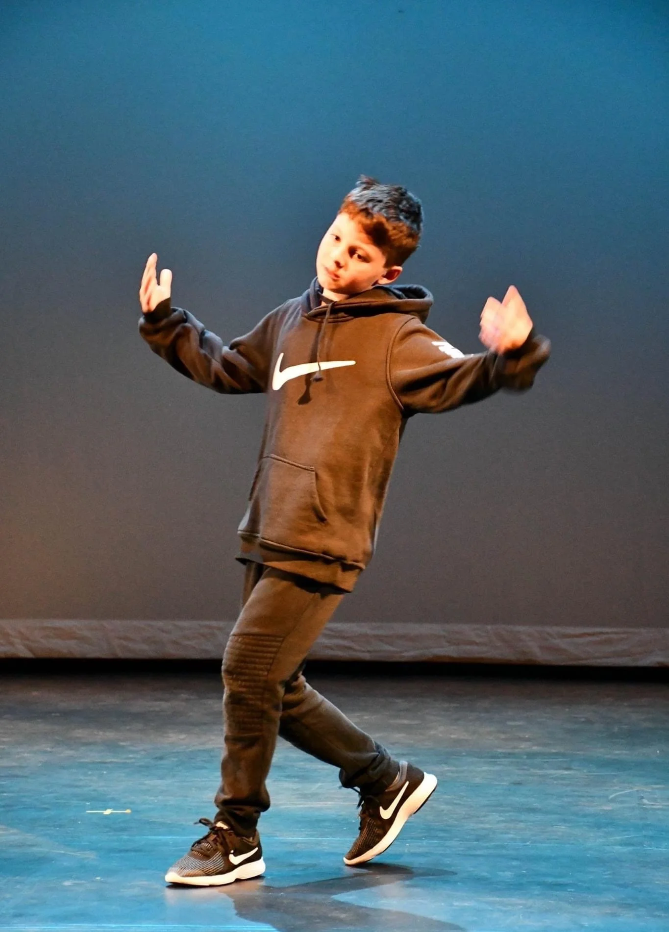 Young boy dancing on stage wearing a black hoodie and black Nike sneakers.