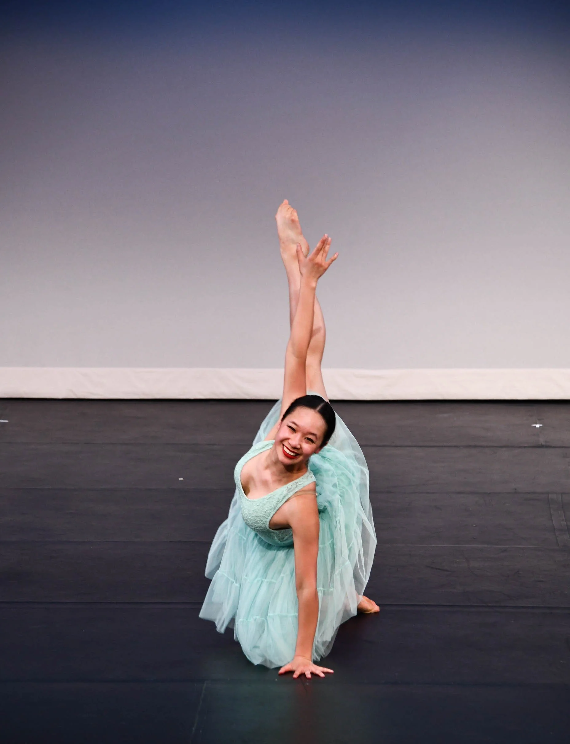 A woman in a light blue dress performing a dance move on stage, smiling at the camera.