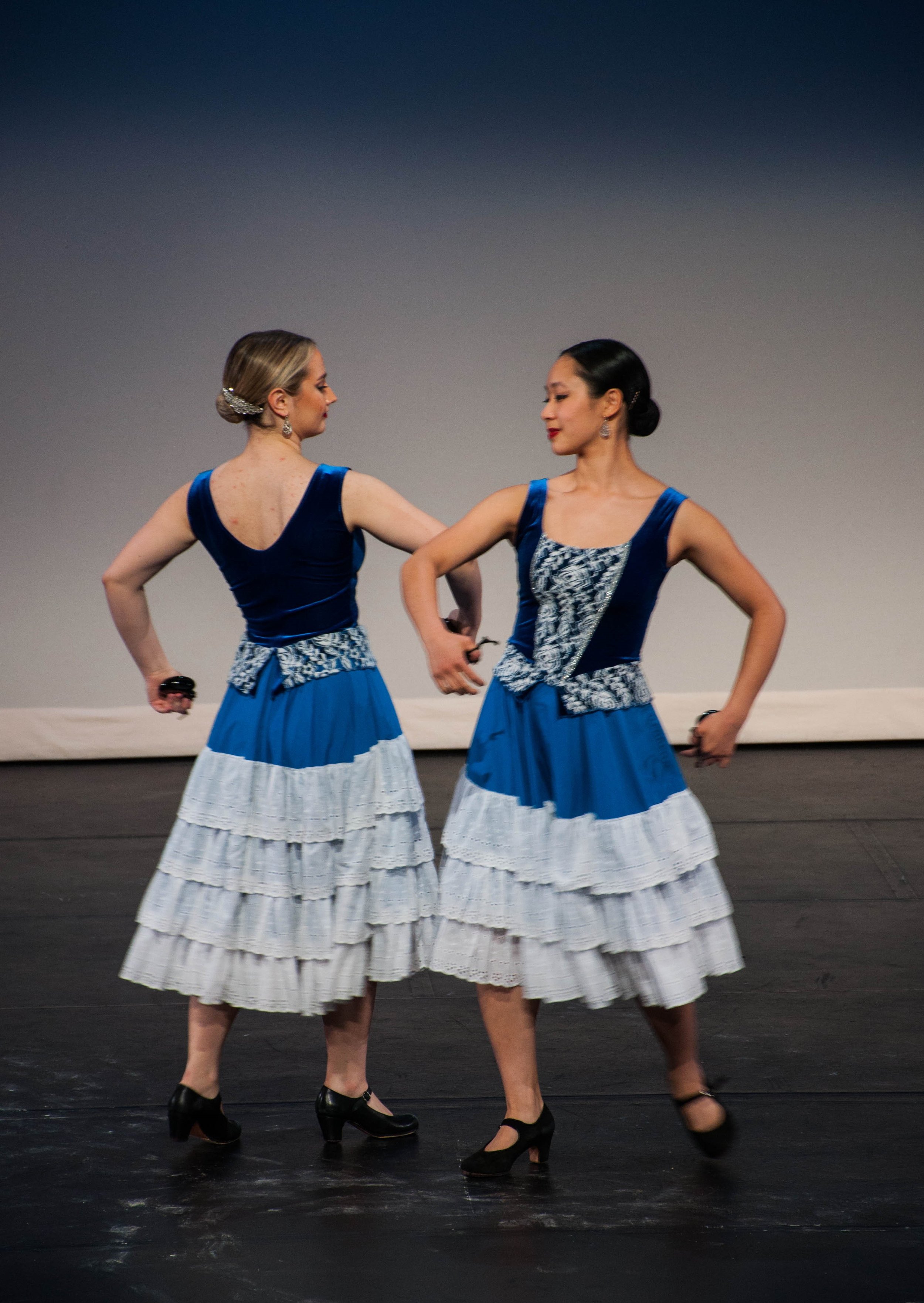 Two women dancing on stage wearing blue and white dresses with ruffled skirts and black heels.