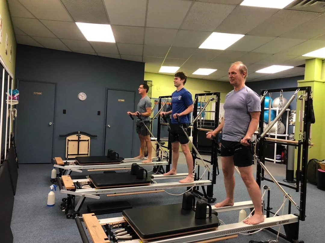 People exercising on Pilates reformer machines in a gym.