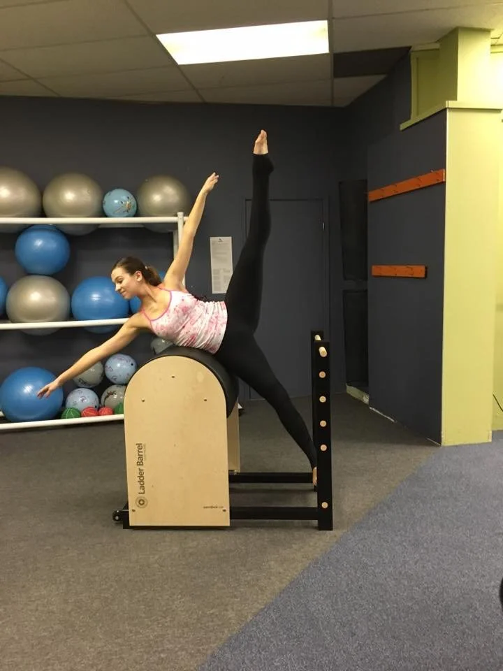 A woman demonstrating a yoga pose on a piece of Pilates equipment in a fitness studio.