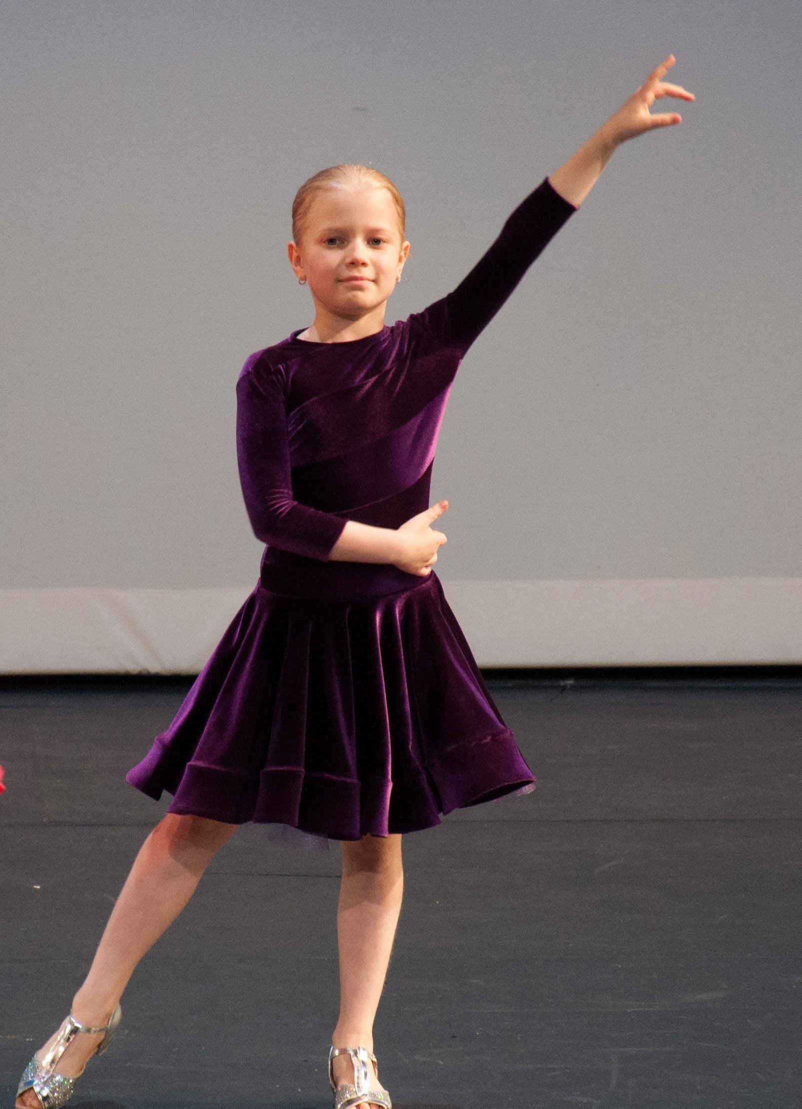 Young girl in a purple velvet dress performing a dance on stage