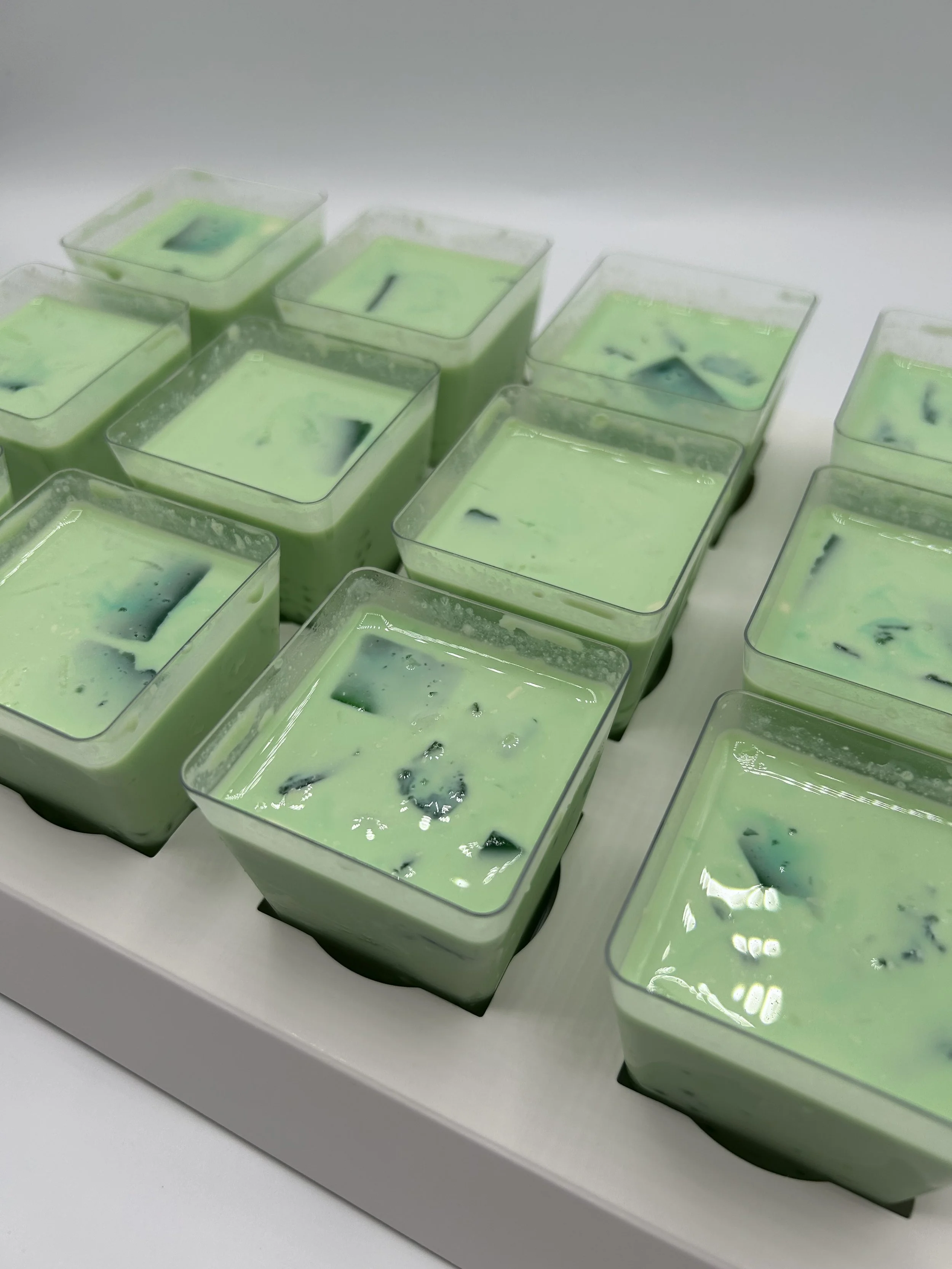 Multiple small square containers filled with green and black marbled drink on a white tray.