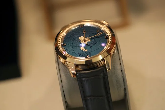 Close-up of a luxury wristwatch with a gold case and black strap, showing a world map on its dial with gold hands.