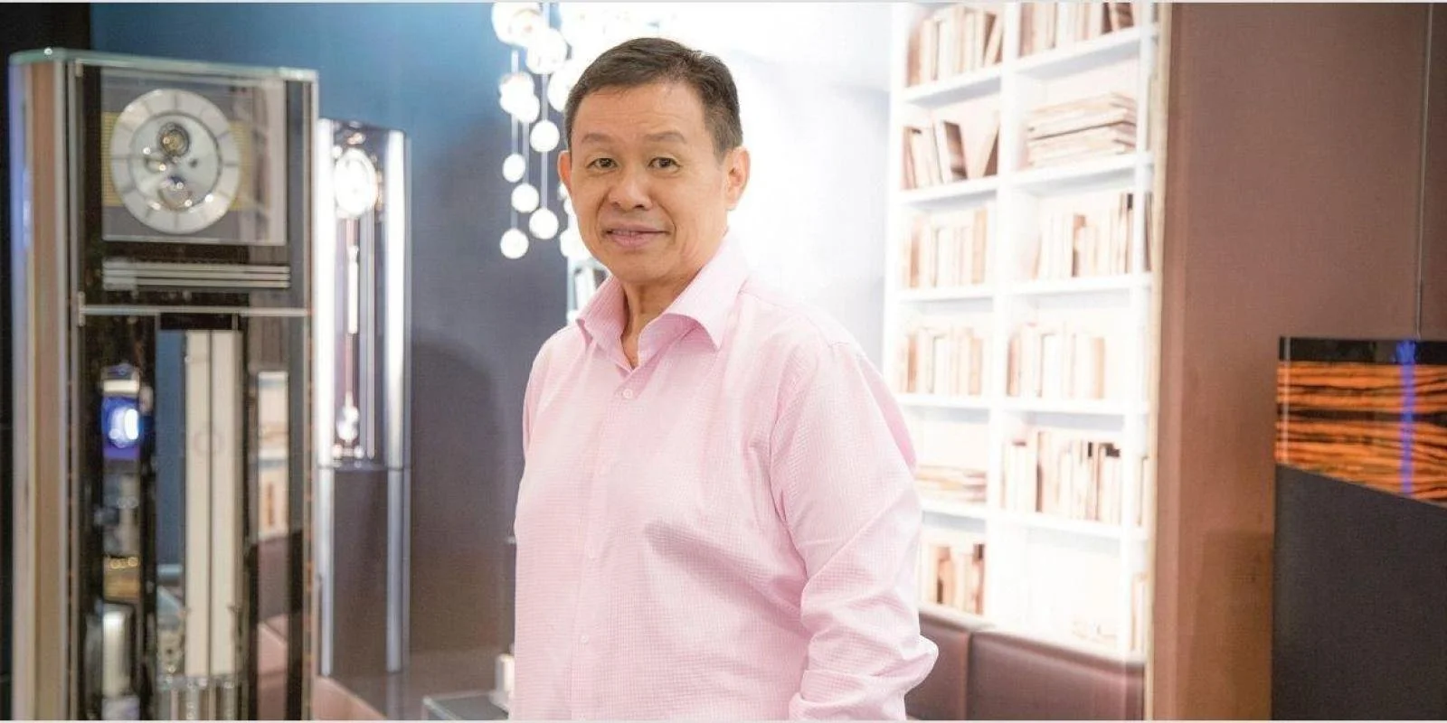 A man in a pink shirt standing in a room with bookshelves and modern decor.