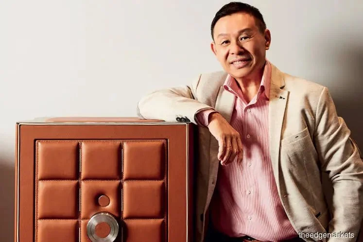 A man in a light beige blazer and pink dress shirt leaning on a large, vintage speaker.