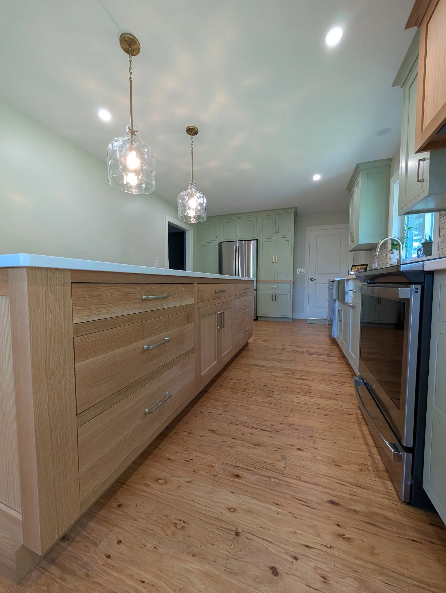 Modern kitchen with wooden cabinets, stainless steel appliances, light green upper cabinets, and pendant lights hanging from the ceiling.