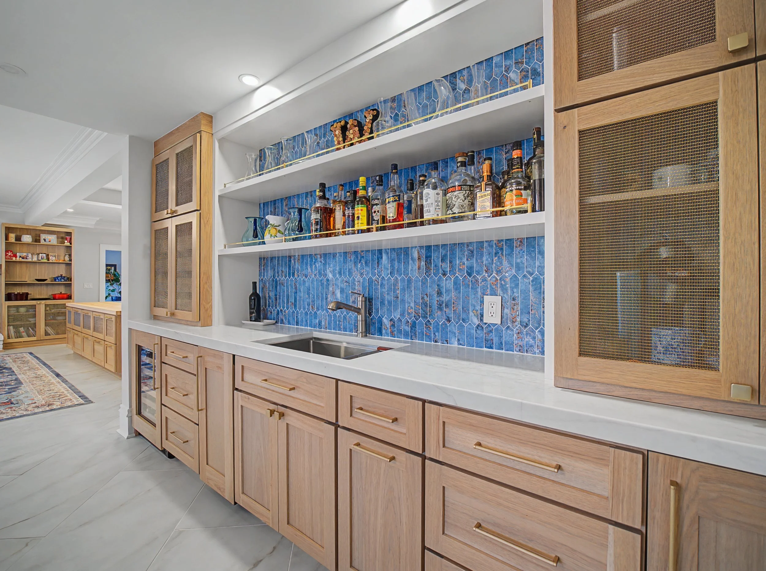 A kitchen area with wooden cabinets, a blue patterned backsplash, and shelves holding glassware and liquor bottles.