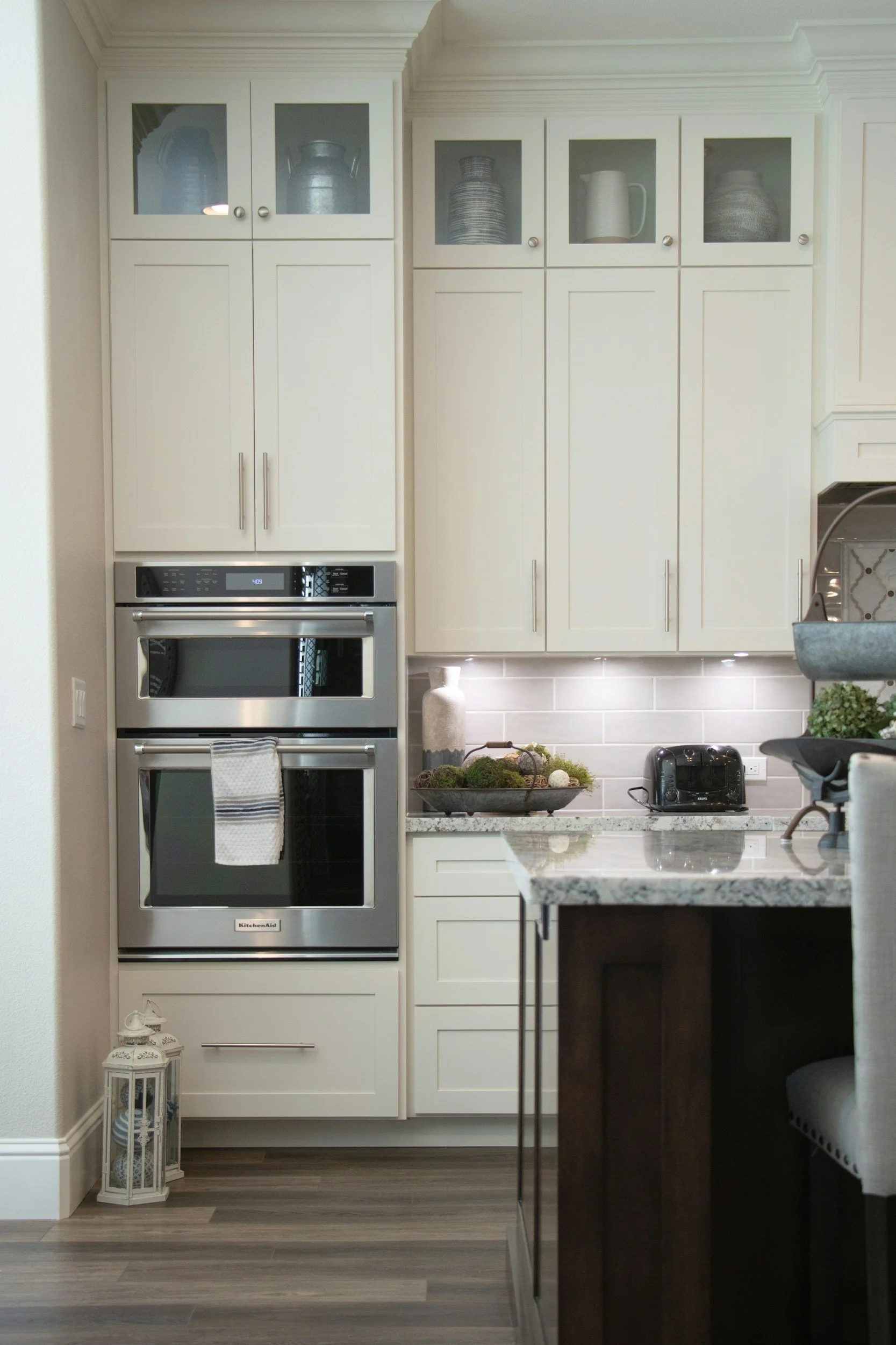 Floor-to-ceiling cream shaker kitchen cabinets with glass fronts and built-in double ovens