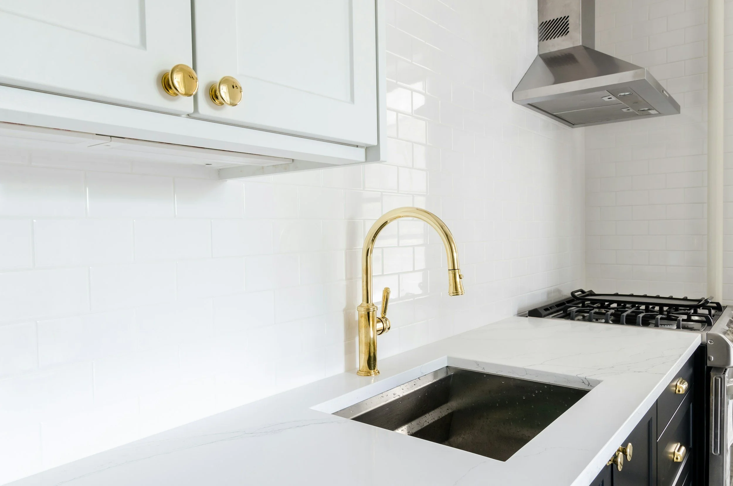White kitchen with brass faucet, subway tile backsplash and quartz countertop