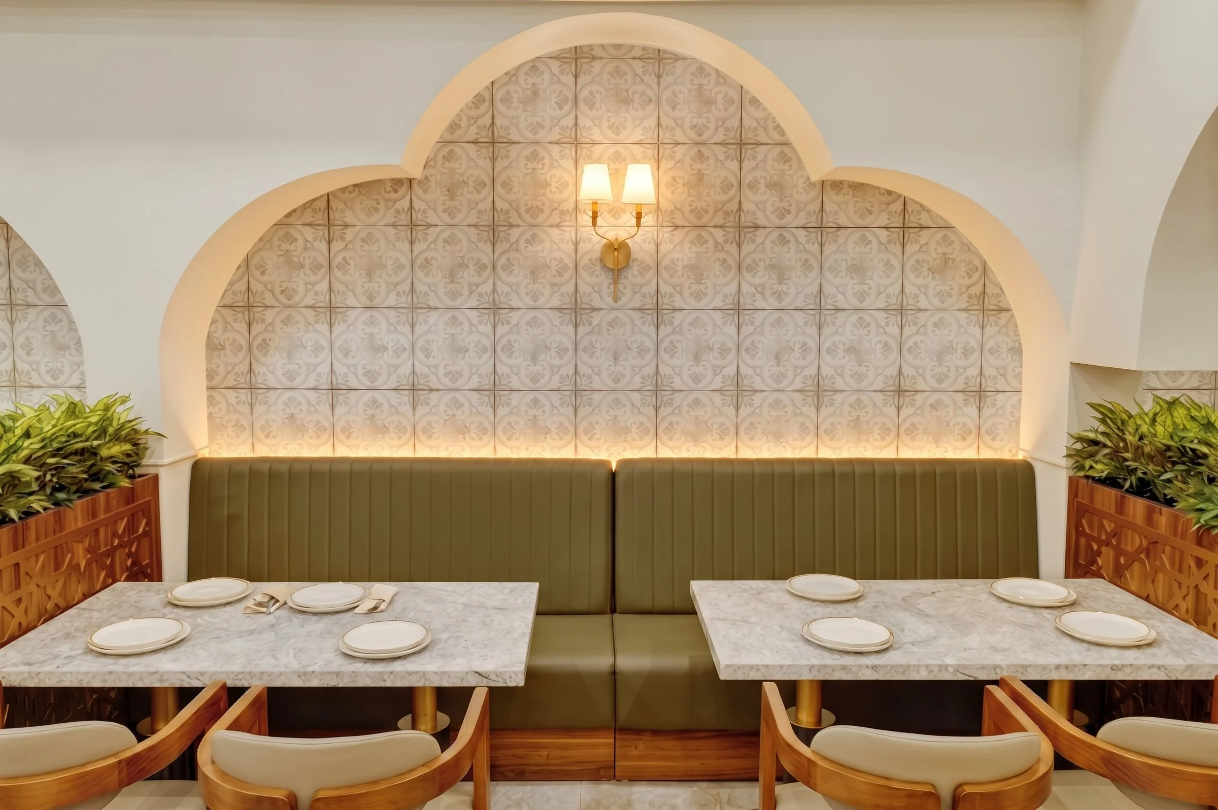 aArched banquette niche with backlit patterned tile, sage green tufted seating and marble tables at Socotra Restaurant, Clifton NJ