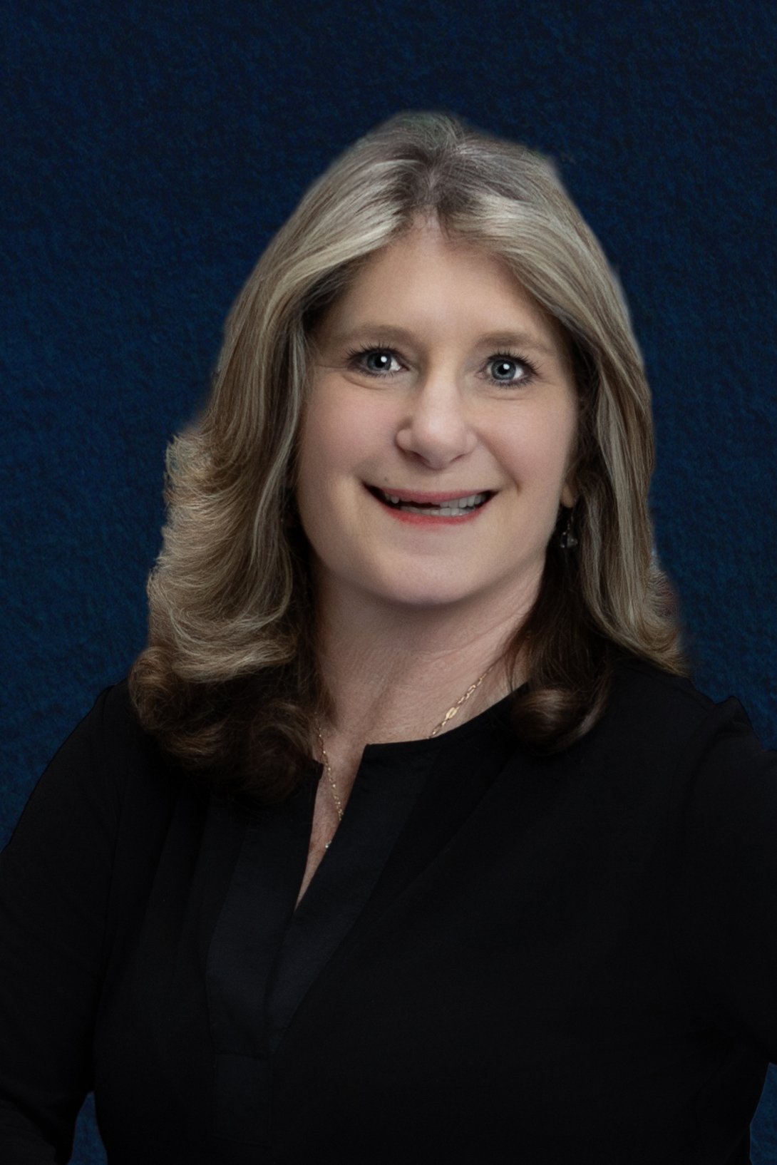 A portrait of a woman with shoulder-length blonde hair, wearing a black top, smiling against a dark blue background.