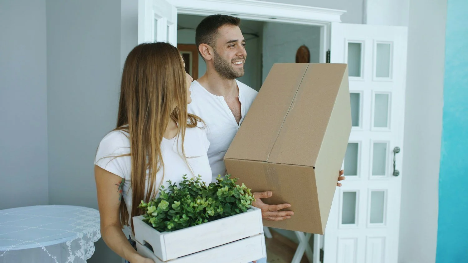 A couple carries moving boxes into a new home - the moment a welcome from new neighbors matters most