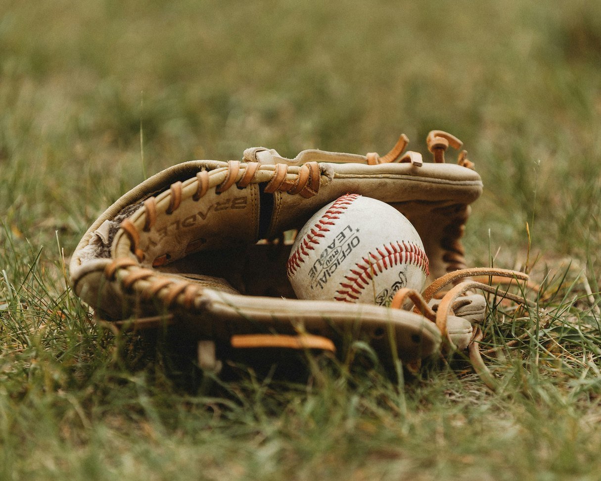 A baseball rests in a worn glove on the grass - an open invitation to play catch with a neighbor