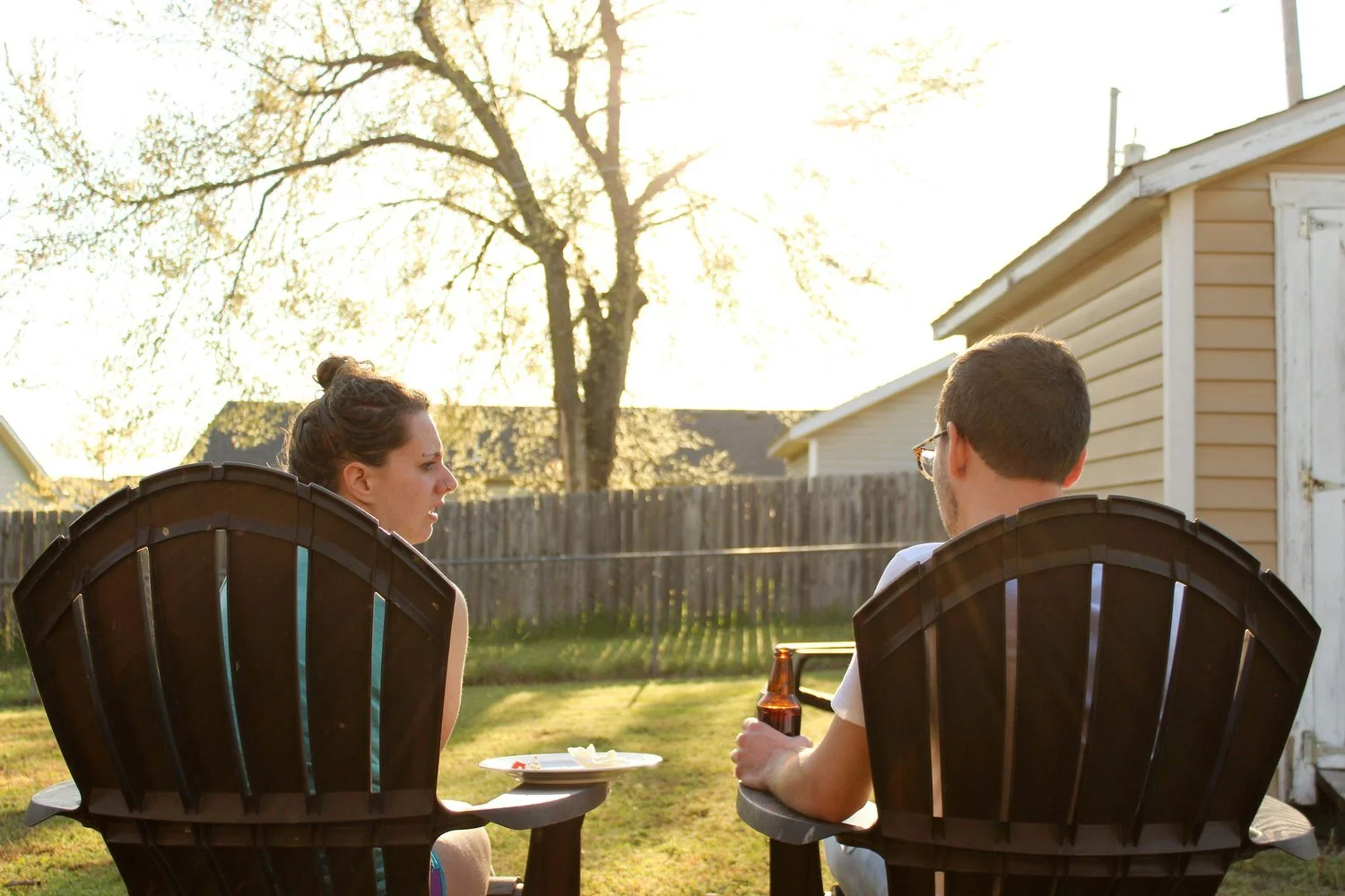 Two neighbors talk in backyard Adirondack chairs on a sunny evening