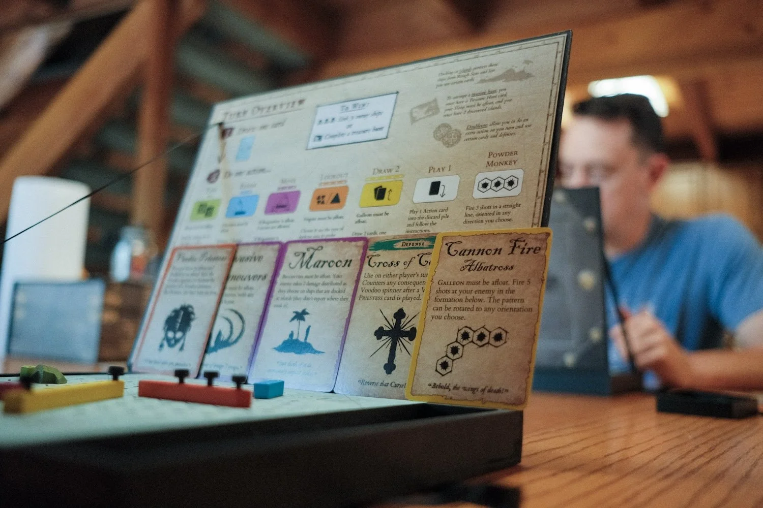 A man sits at a table, deeply immersed in a board game, surrounded by game pieces and a lively atmosphere.