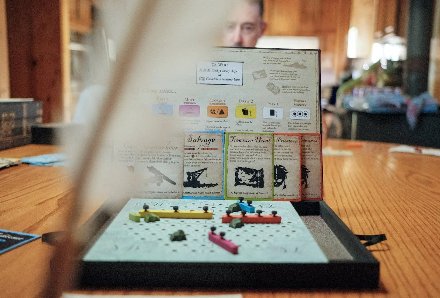 A man enjoys a board game at a table, deep in thought as he strategizes his next move with game pieces around him.