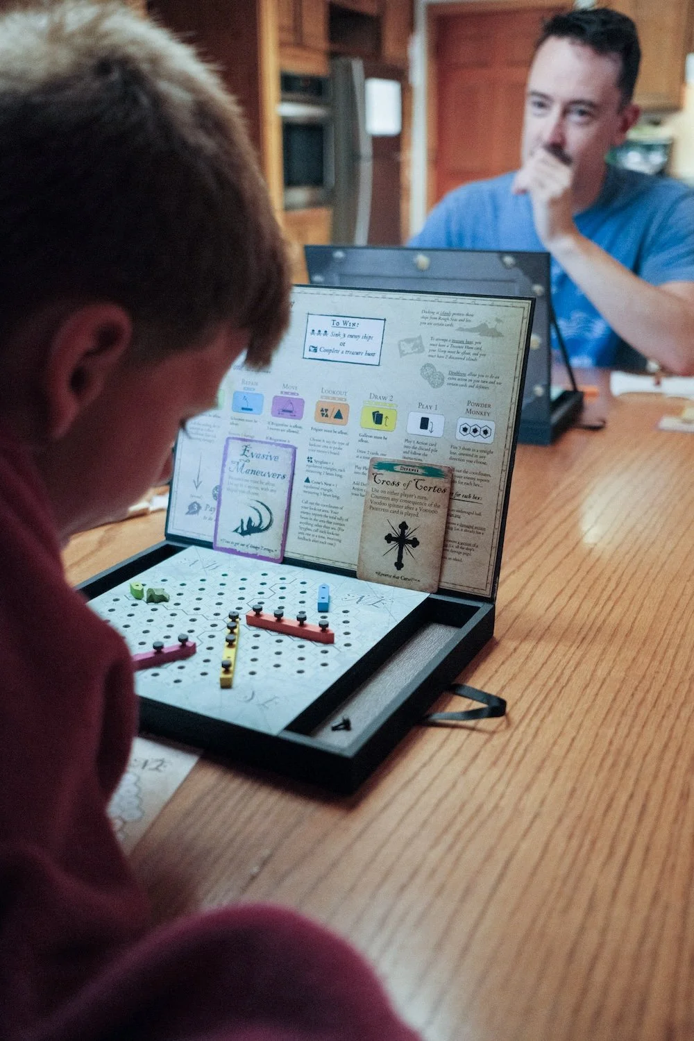 A young boy and his uncle are engaged in a board game, surrounded by colorful game pieces and a joyful atmosphere.