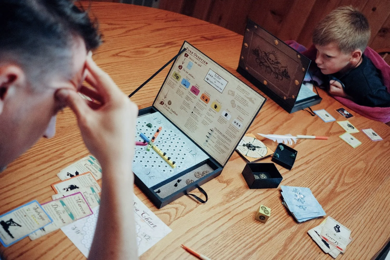 A man and a boy are focused at a table, planning their next move in a vibrant board game.