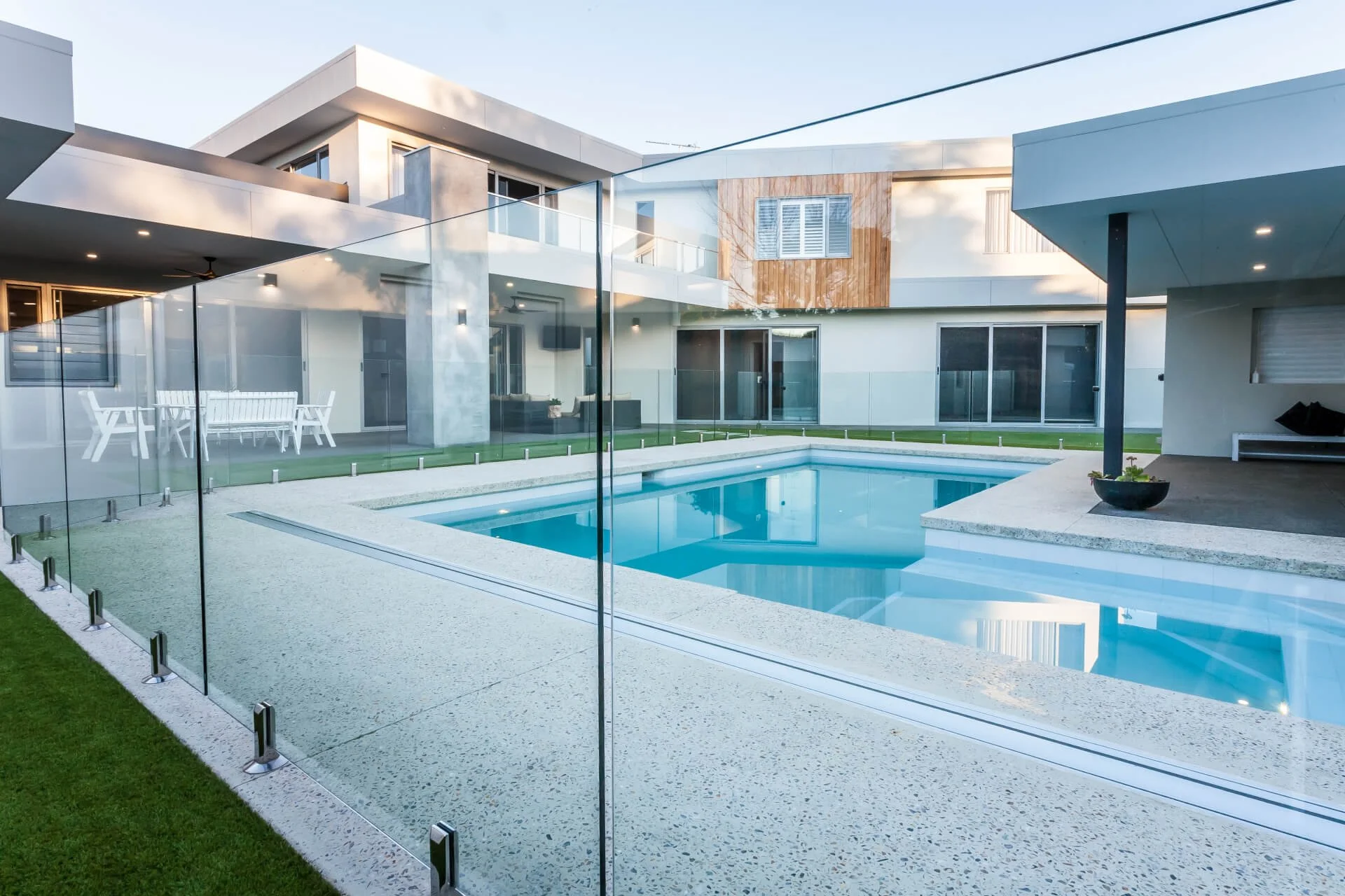 Modern house with a swimming pool, glass fencing, outdoor dining area, and second-floor balcony.
