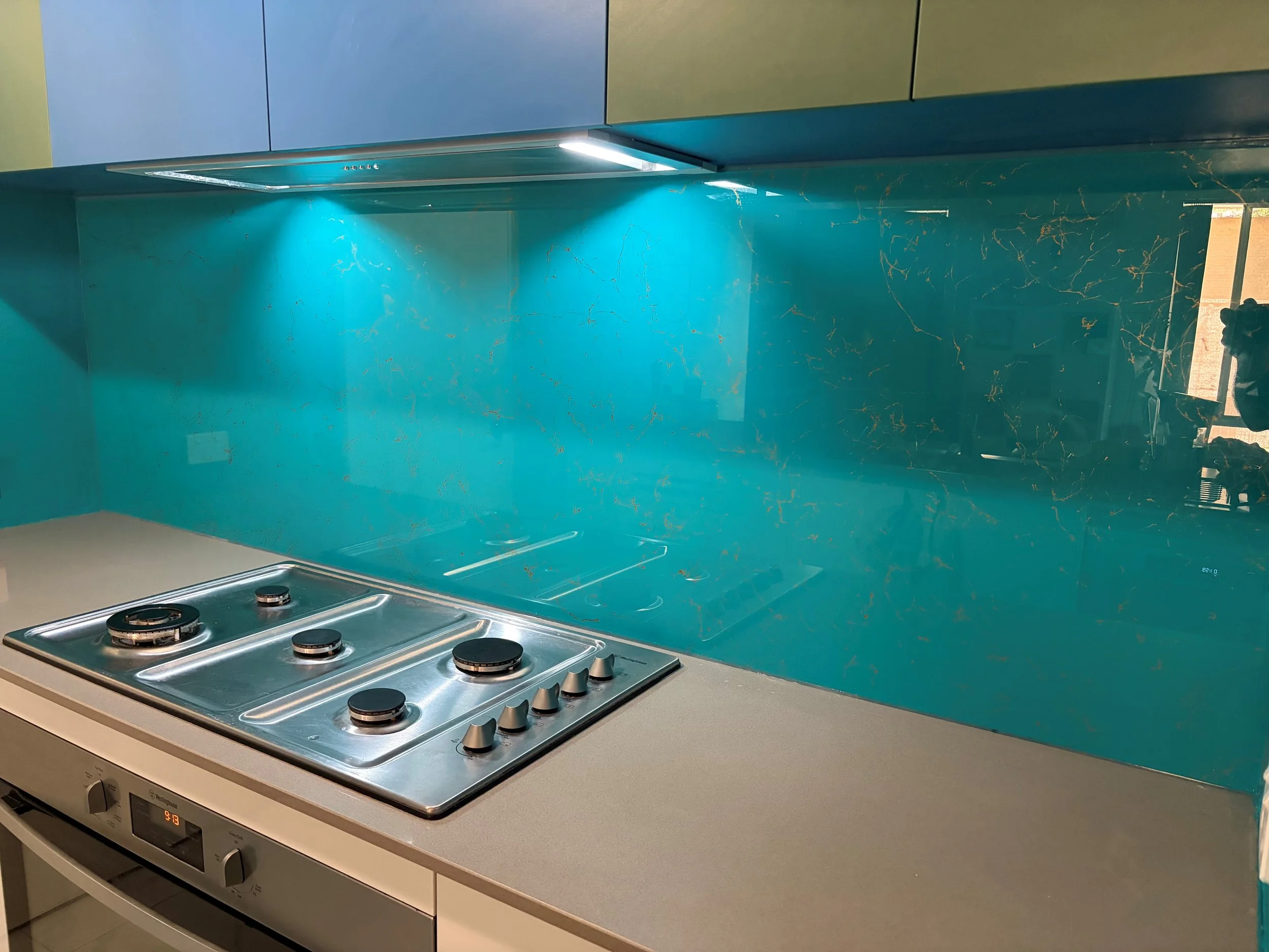 Modern kitchen stove with four burners, a digital display, and a turquoise backsplash with gold veining.