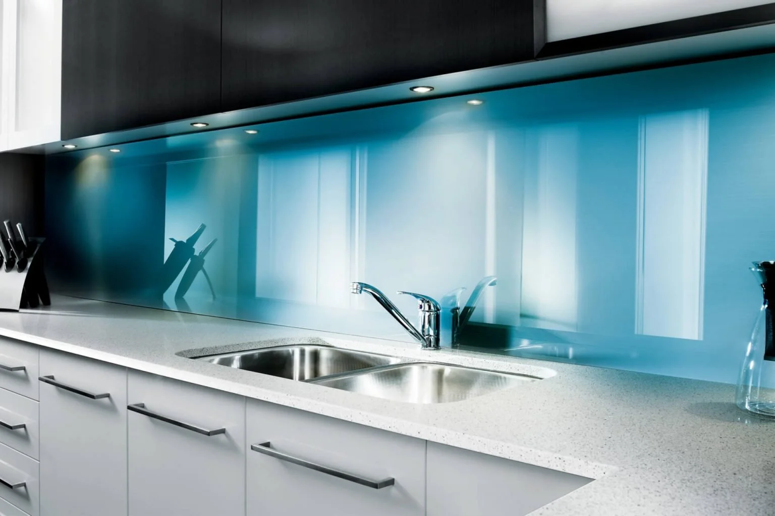 Modern kitchen with white countertop, stainless steel sink, black knives, and a blue glass backsplash