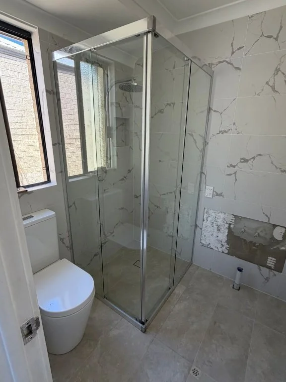 Empty bathroom with a glass shower enclosure, a toilet, and unfinished wall with exposed plumbing and fixtures.
