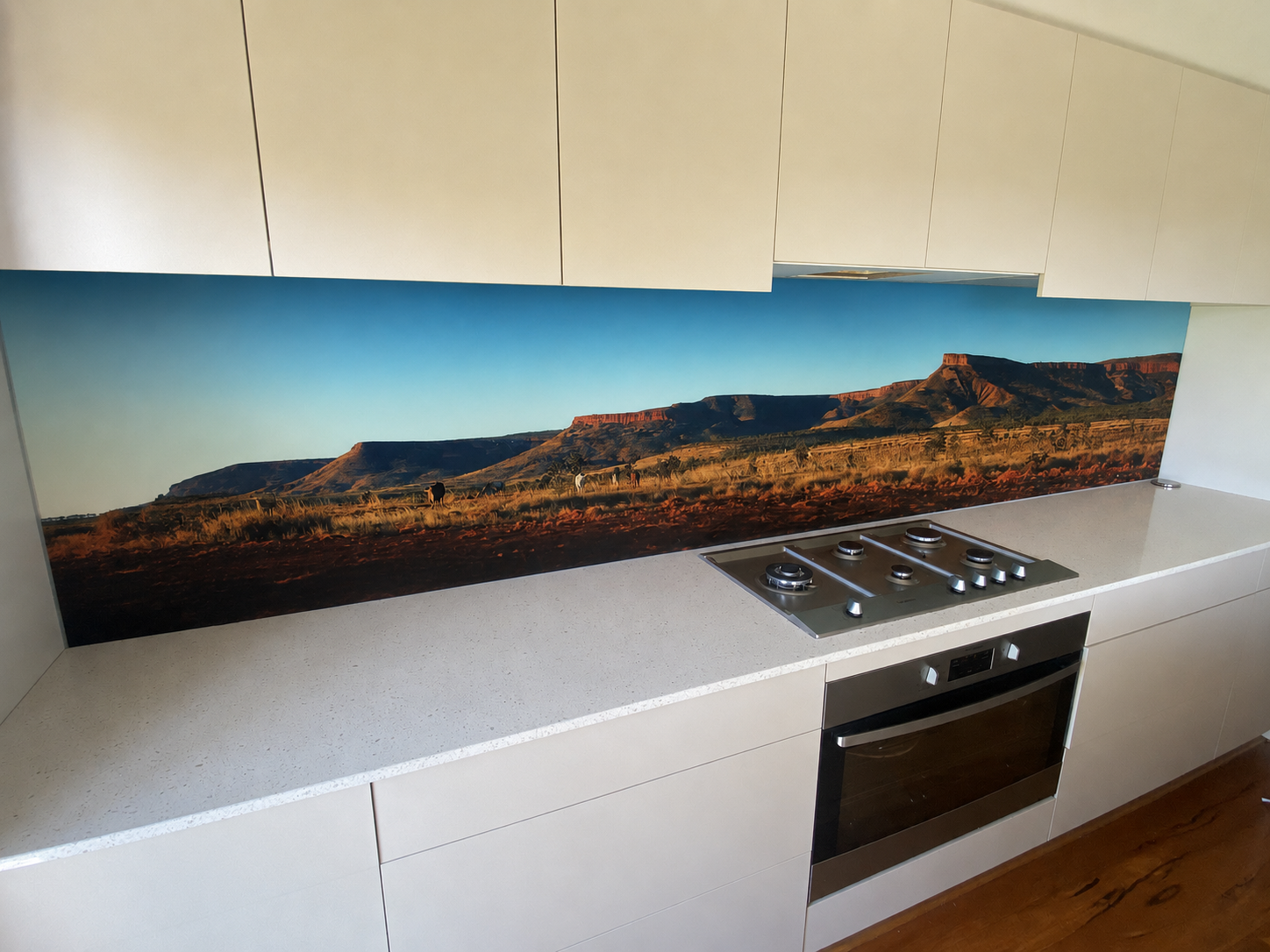 Kitchen countertop with a desert landscape backsplash featuring mesas and small animals, under beige overhead cabinets.