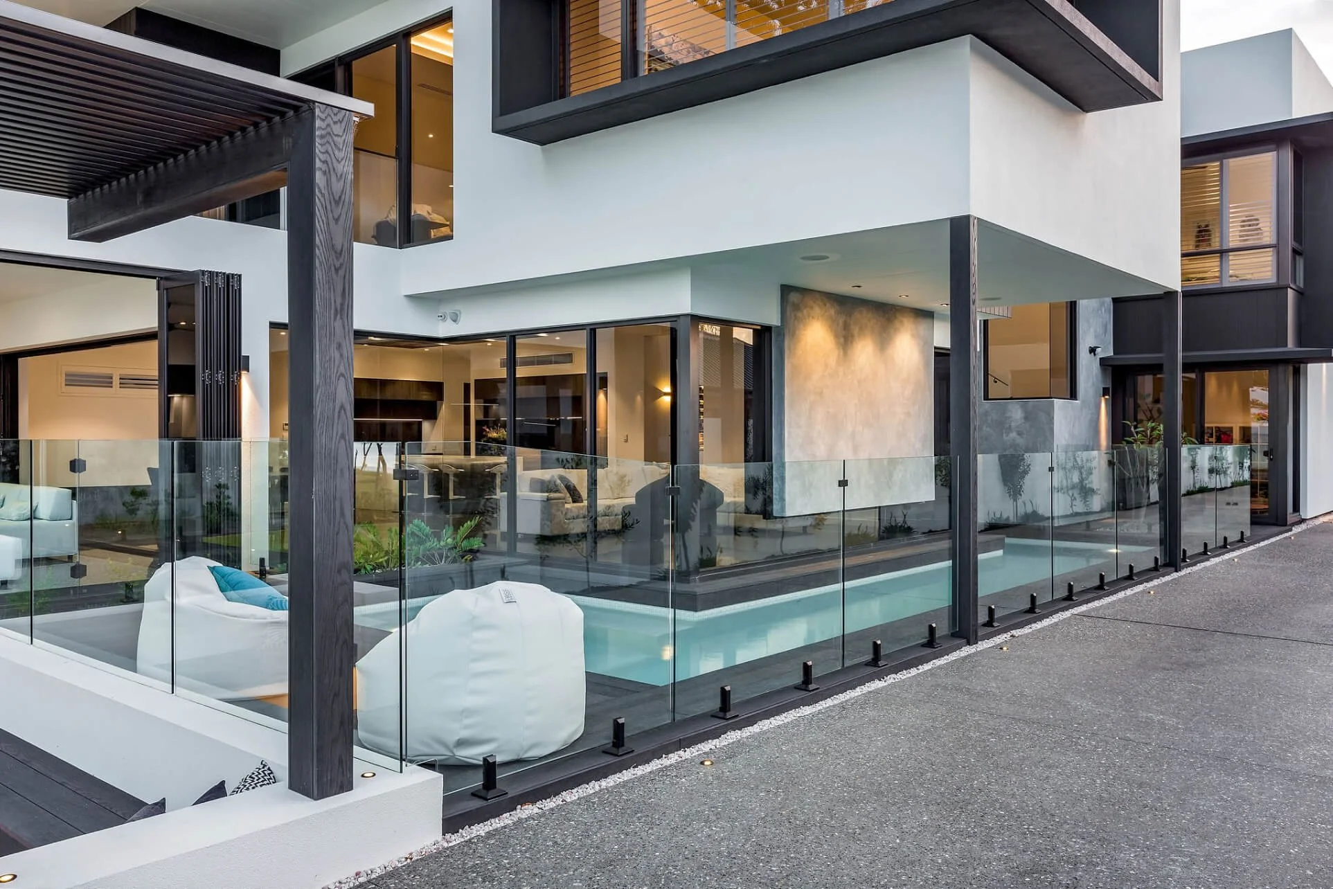 Modern multi-story house with large glass windows and balcony, glass railing around a swimming pool, and contemporary exterior design.