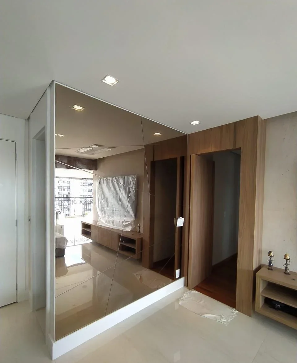 Room with a large mirrored wall reflecting an outdoor balcony, a wooden cabinet, and a partially covered window.