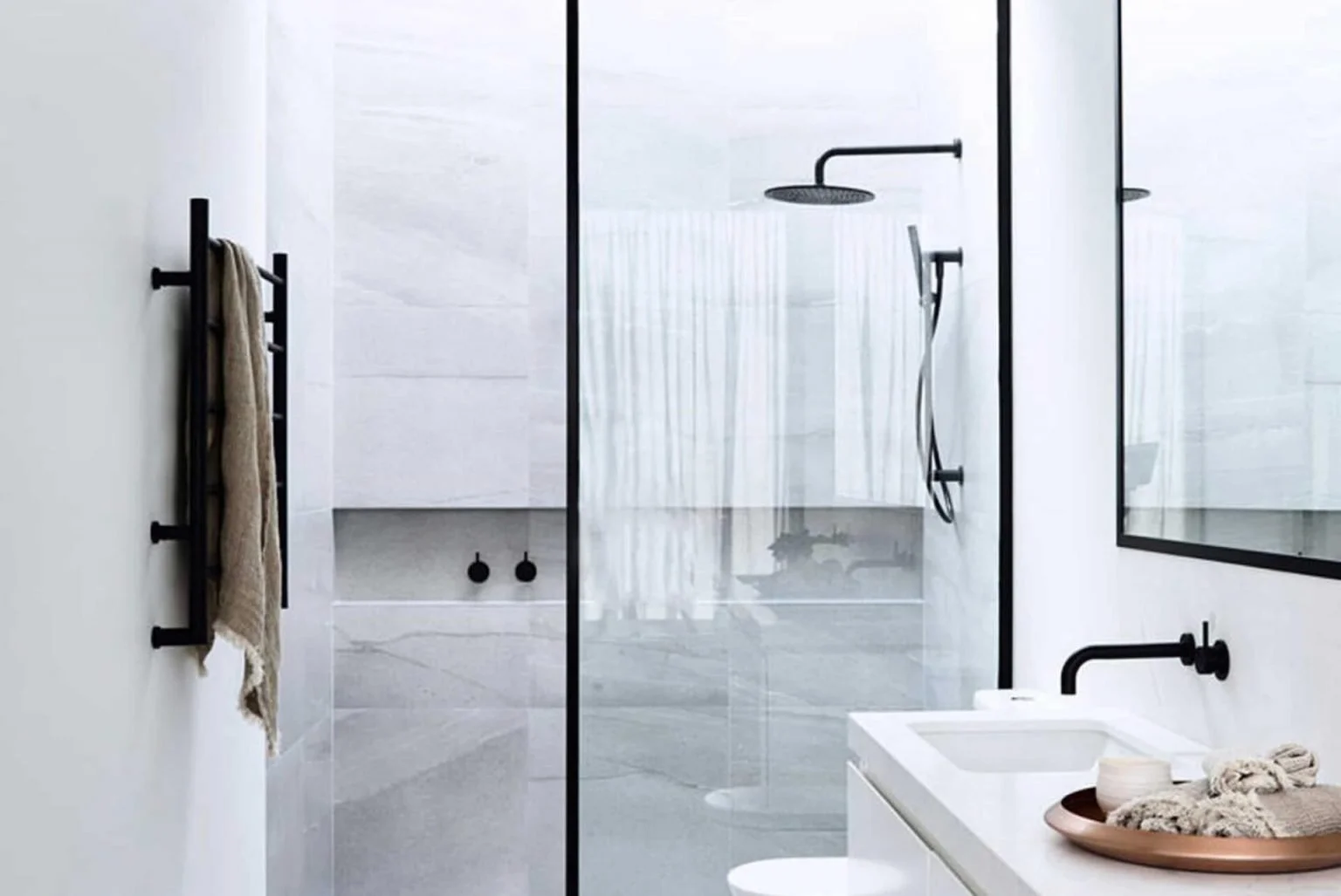 Modern bathroom with a walk-in shower enclosed by clear glass with black framing, a black rain showerhead, and a handheld shower, a white vanity with a black faucet, a mirror, and a towel rack with towels.