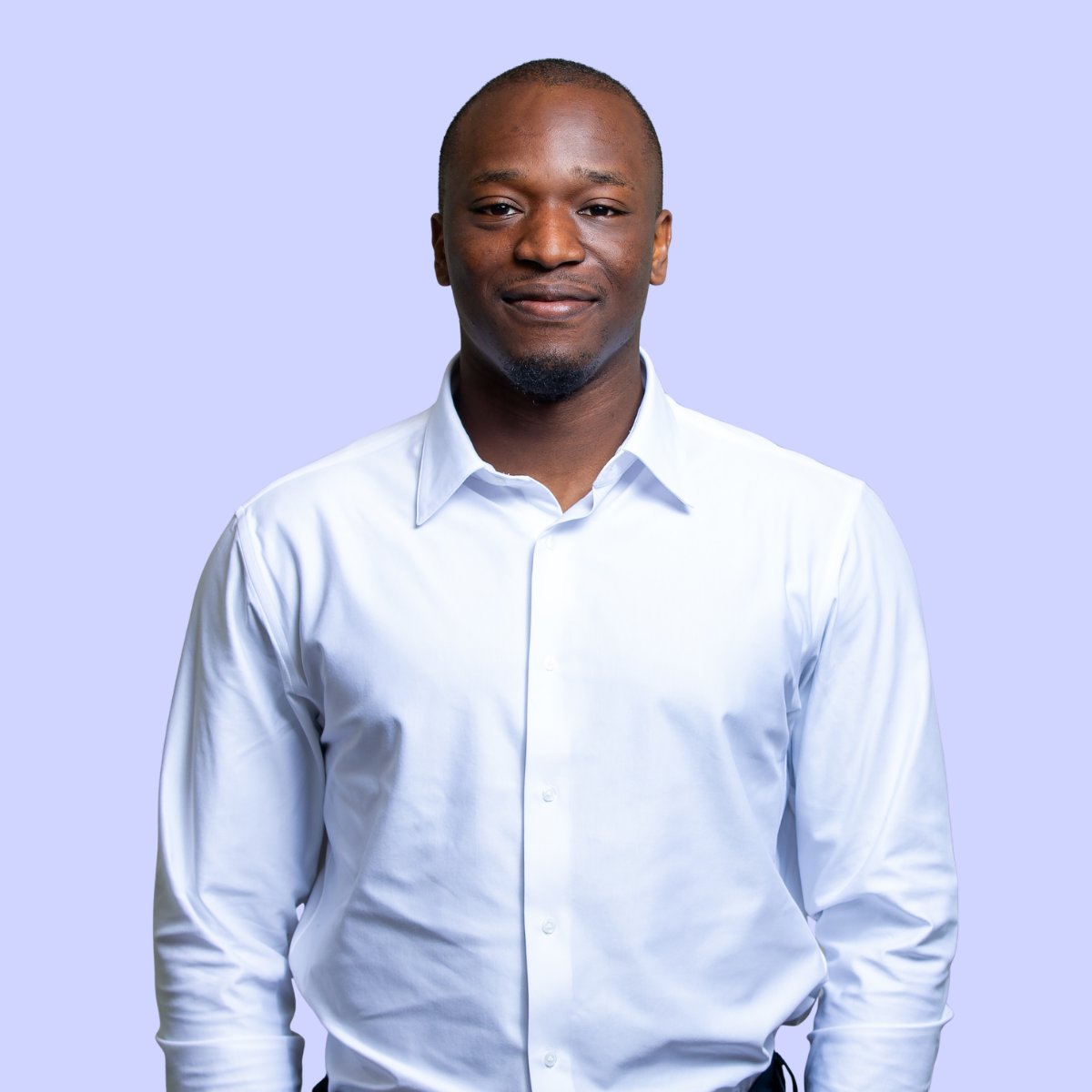 Person wearing a beige sweater and white shirt standing with arms crossed against a peach background.