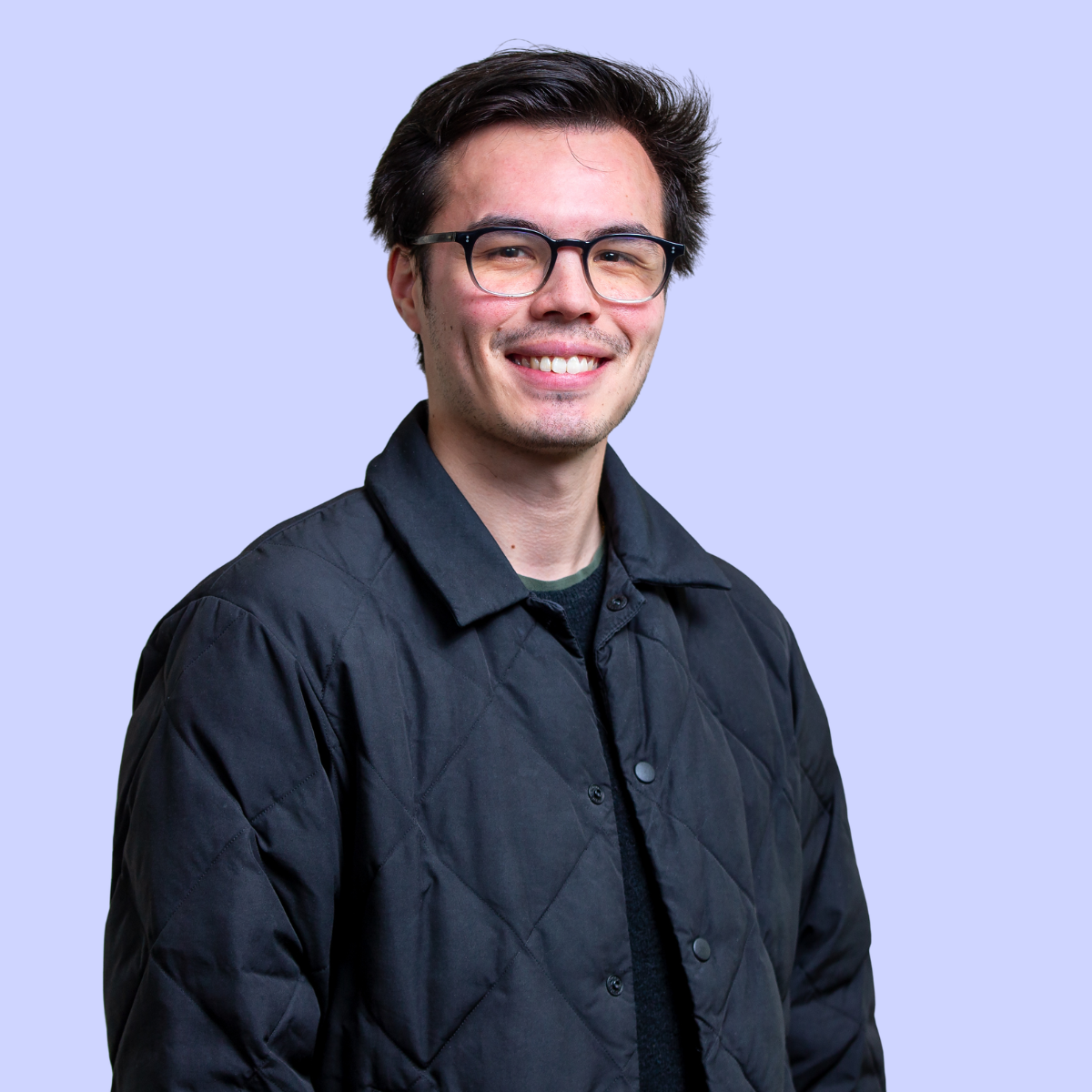 Anthony wearing glasses and a brown pullover against a blue background.